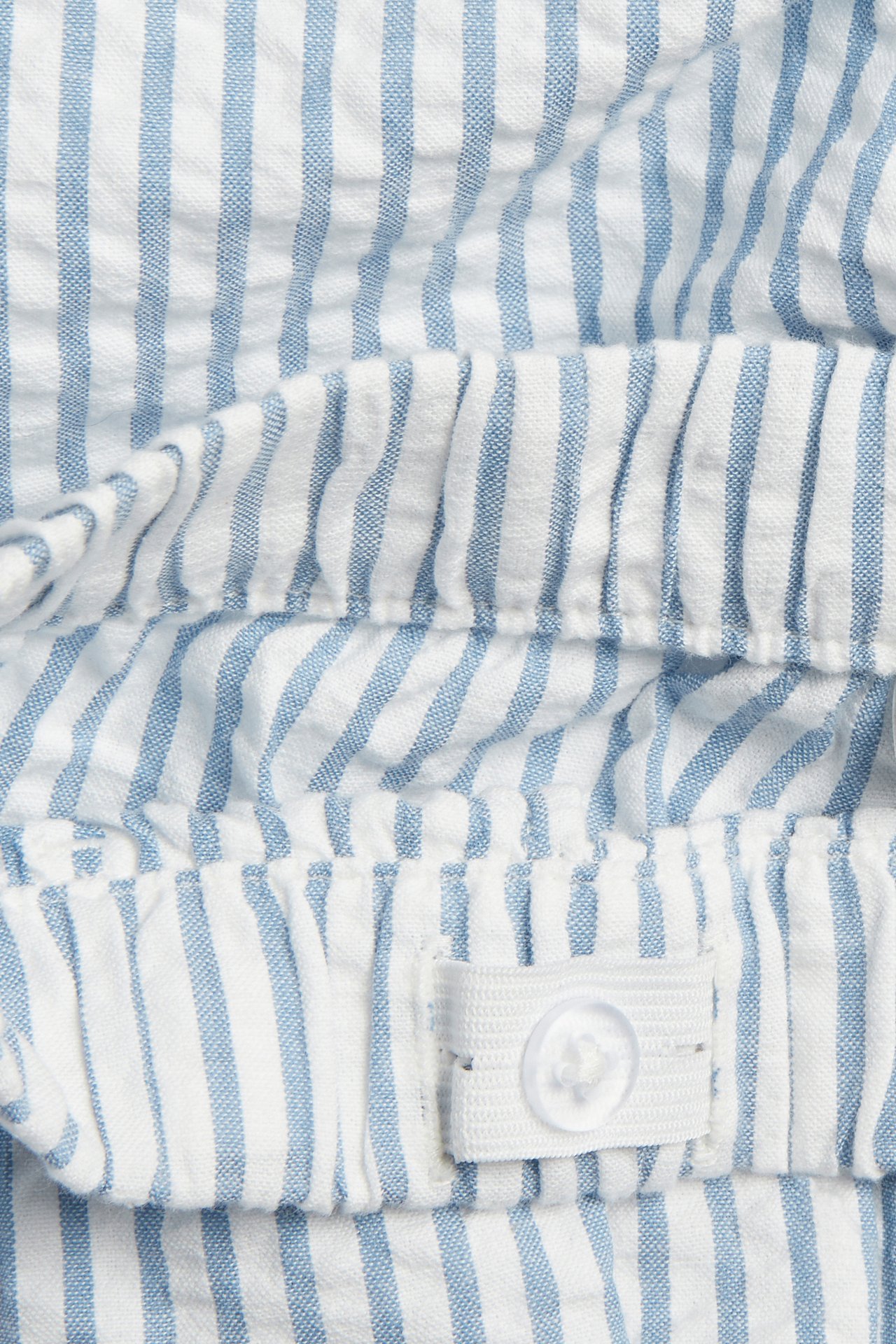 Lähikuva sinivalkoraidallisista puuvillashortseista, joissa joustovyötärö, säädettävä nappi.