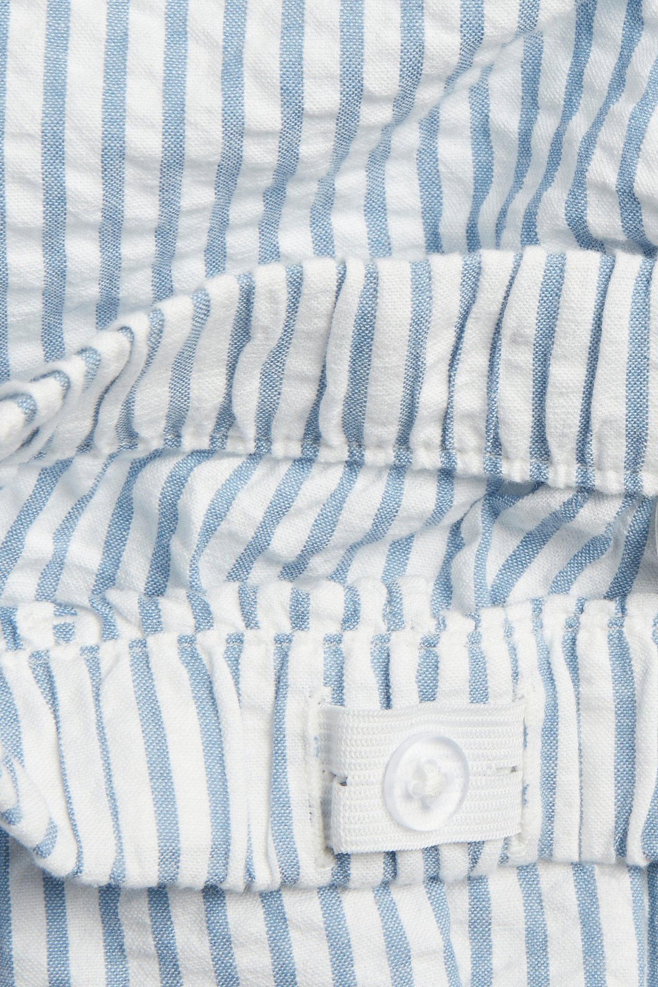 Zbliżenie na bawełniane szorty w niebiesko-białe paski z elastycznym pasem, regulowanym guzikiem.