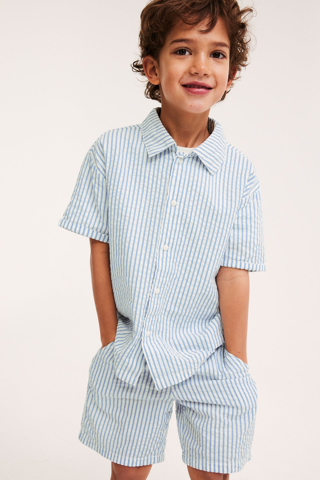 Widok z przodu: dziecko w niebiesko-białych pasiastych szortach seersucker i pasującej koszuli.