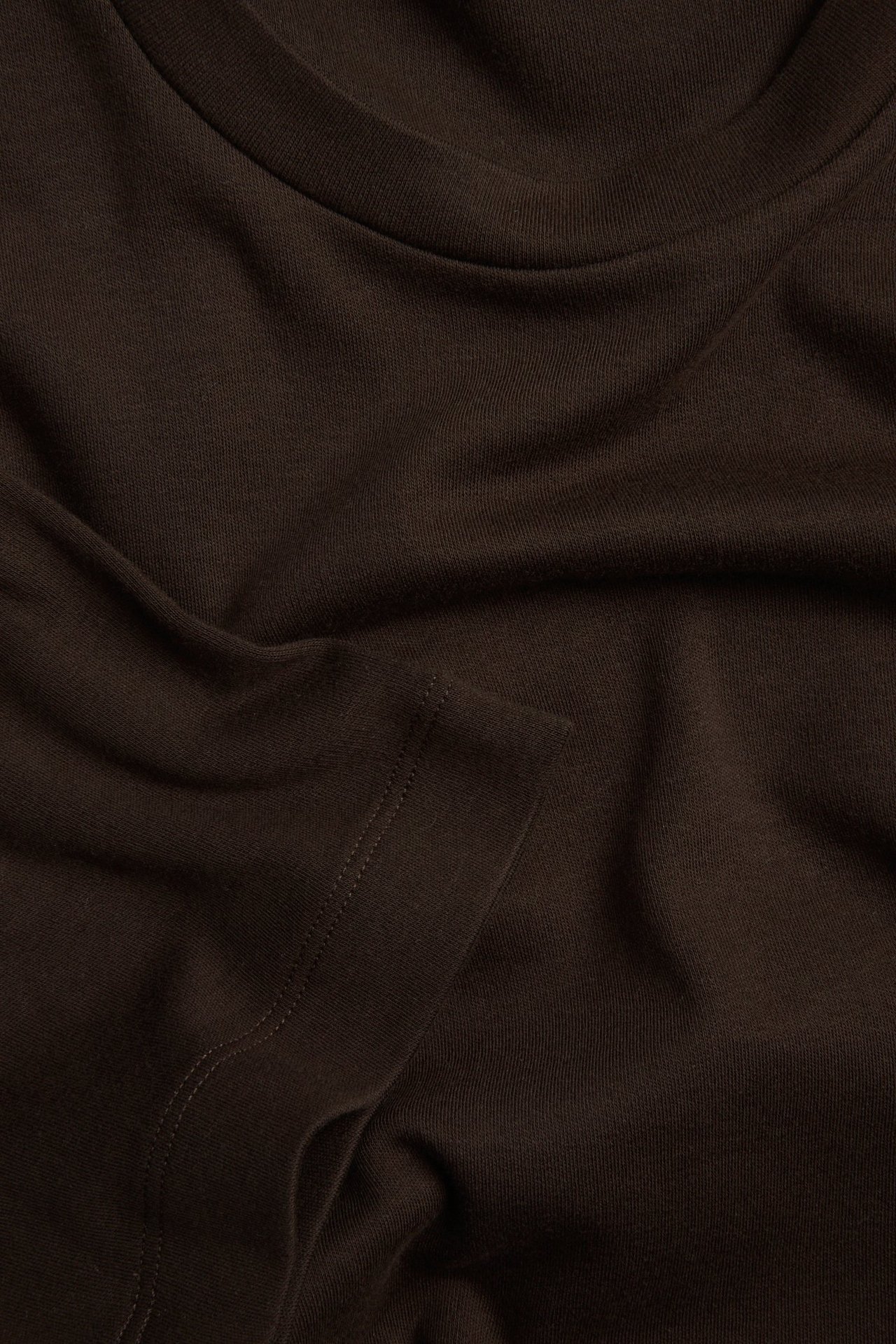 Lähikuva tummanruskeasta, lyhytmallisesta puuvillat-paidasta pyöreällä kaula-aukolla ja lyhyillä hihoilla.