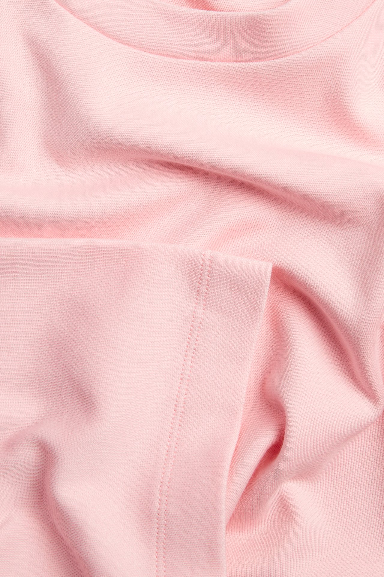 Lähikuva vaaleanpunaisesta puuvillaisesta t-paitakankaasta; tekstuuri, pääntie ja ommeltu sauma näkyvät.