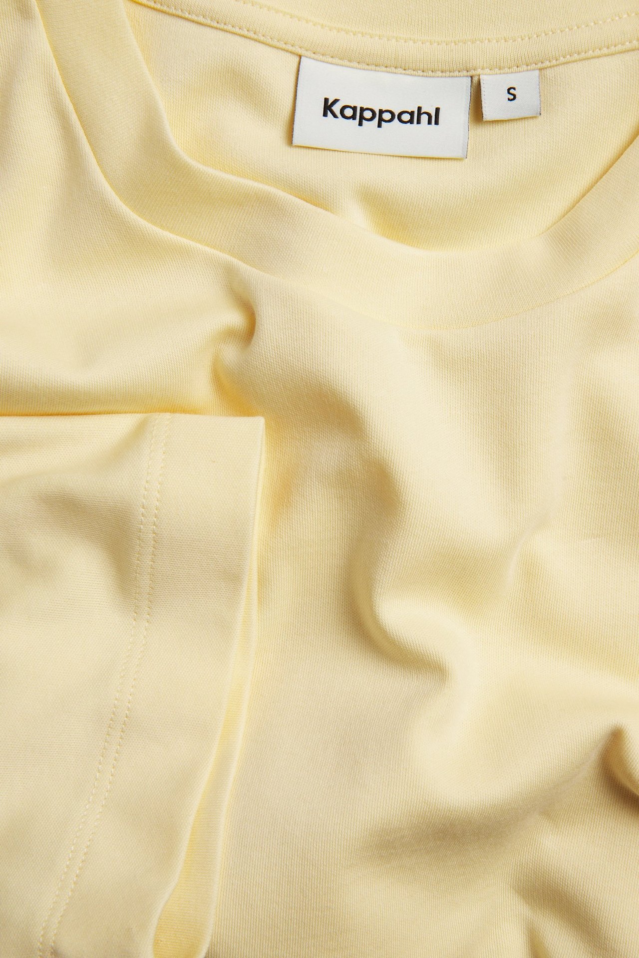 Zbliżenie na jasnożółty, jednokolorowy, krótki T-shirt bawełniany, widoczny kołnierz i rękaw.