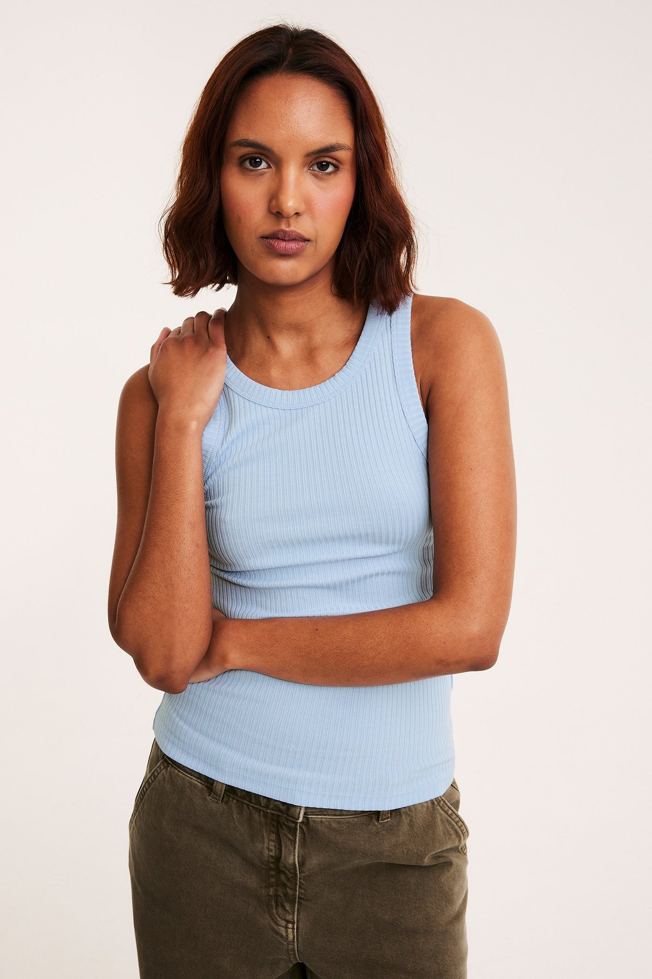 Frontvy av en kvinna i ett ljusblått ribbat linne och olivgröna byxor.