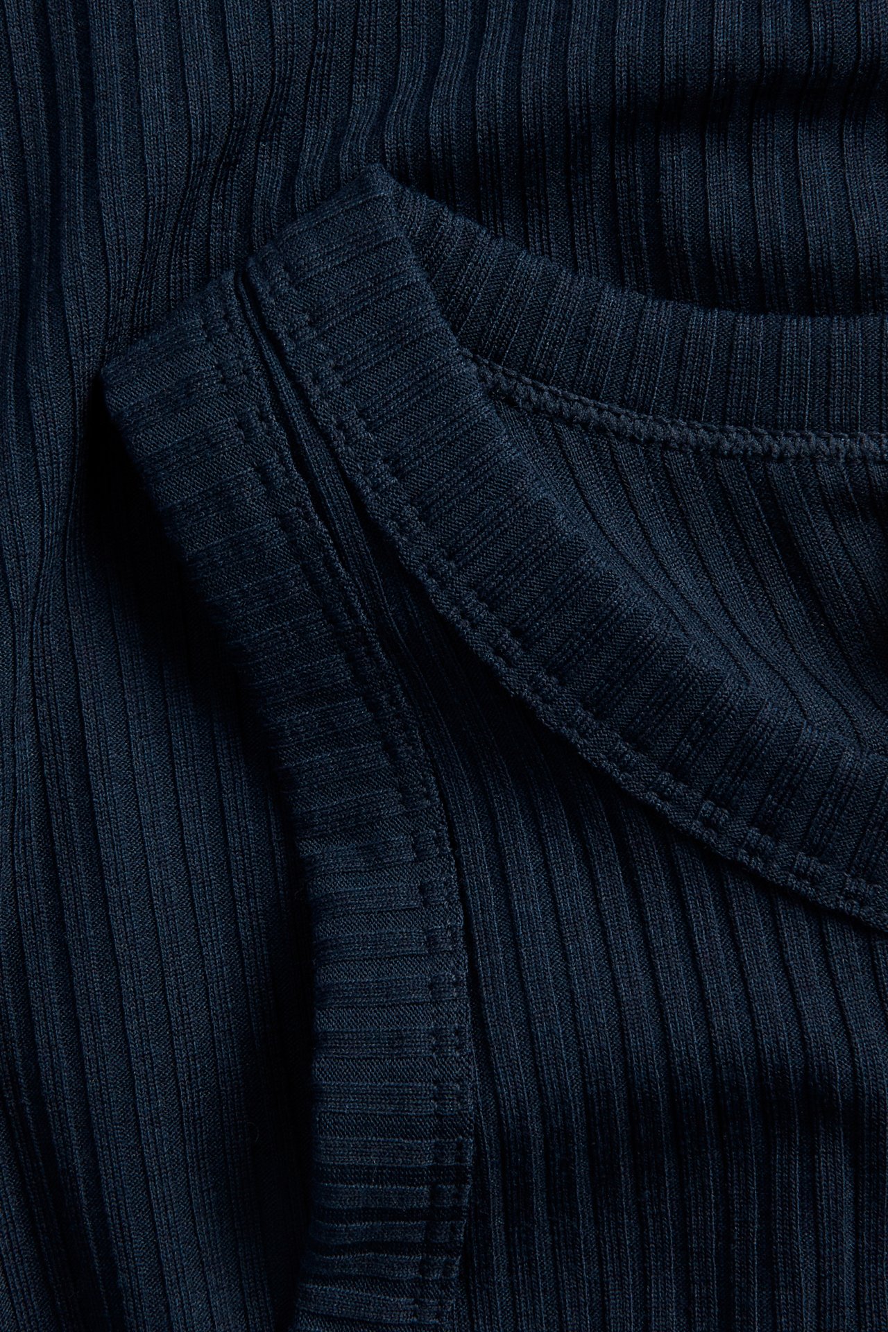 Lähikuva tummansinisestä ribatusta topista, jossa näkyvät tikkaukset.