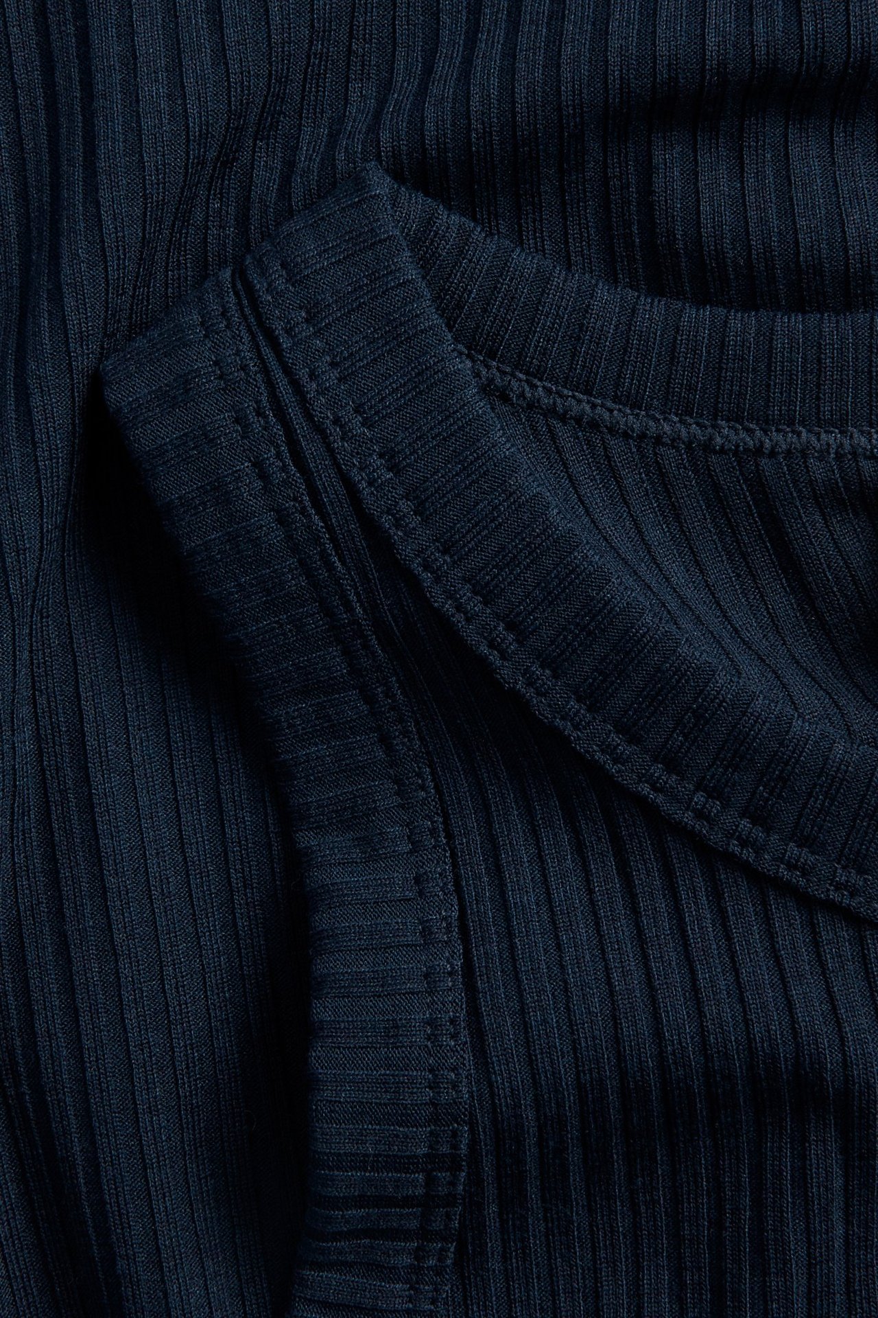 Lähikuva tummansinisestä ribatusta topista, jossa näkyvät tikkaukset.