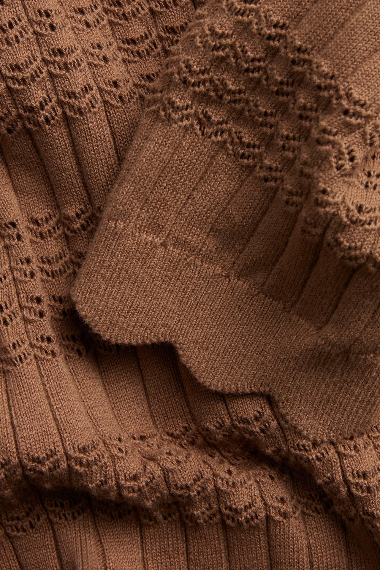 Zbliżenie na brązowy bawełniany top z krótkim rękawem, z prążkowanym ażurowym wzorem i falistym brzegiem.