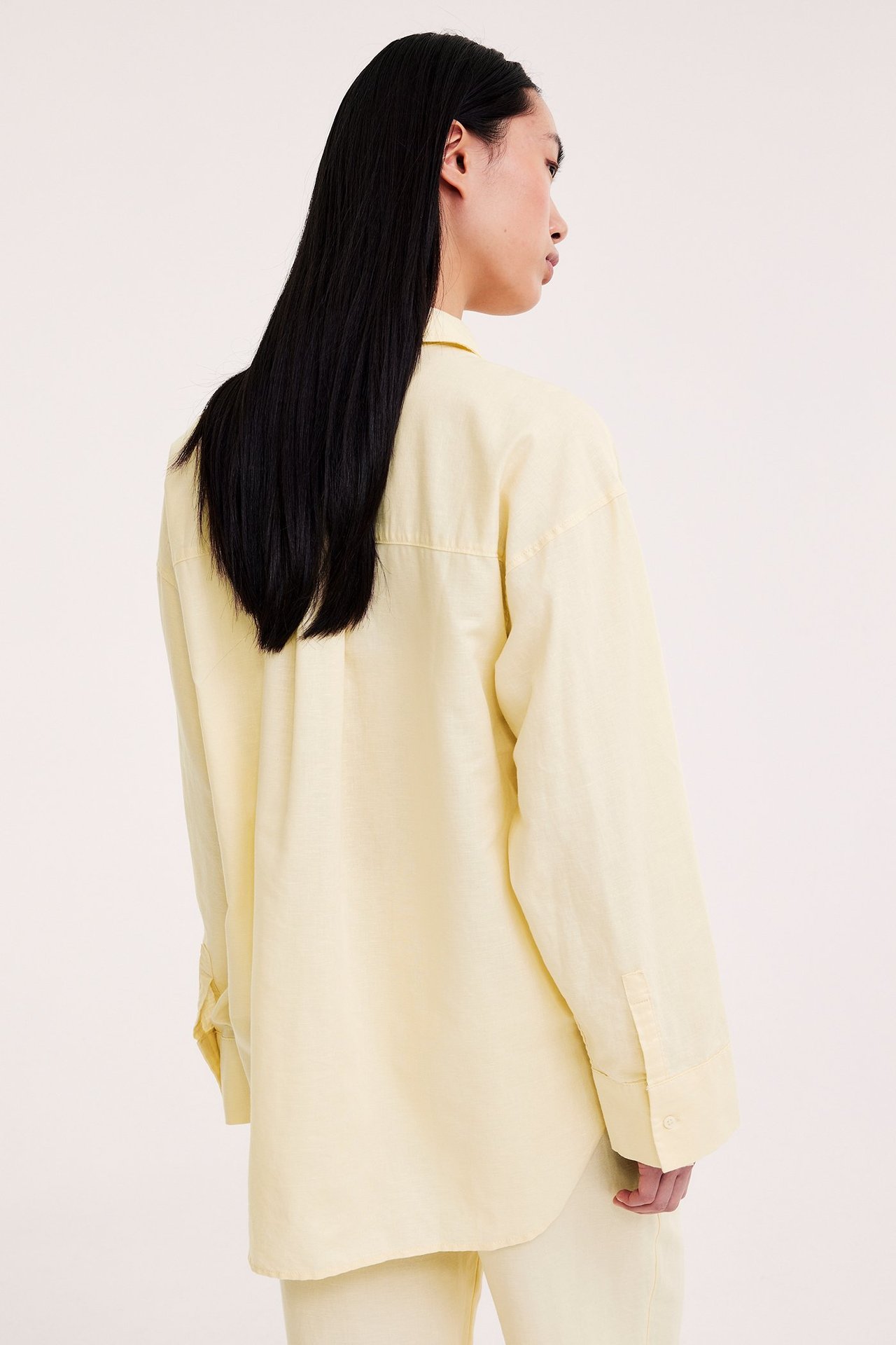 Rygg-sidevisning av en kvinne i en oversized lys gul linblanding skjorte og matchende bukser.