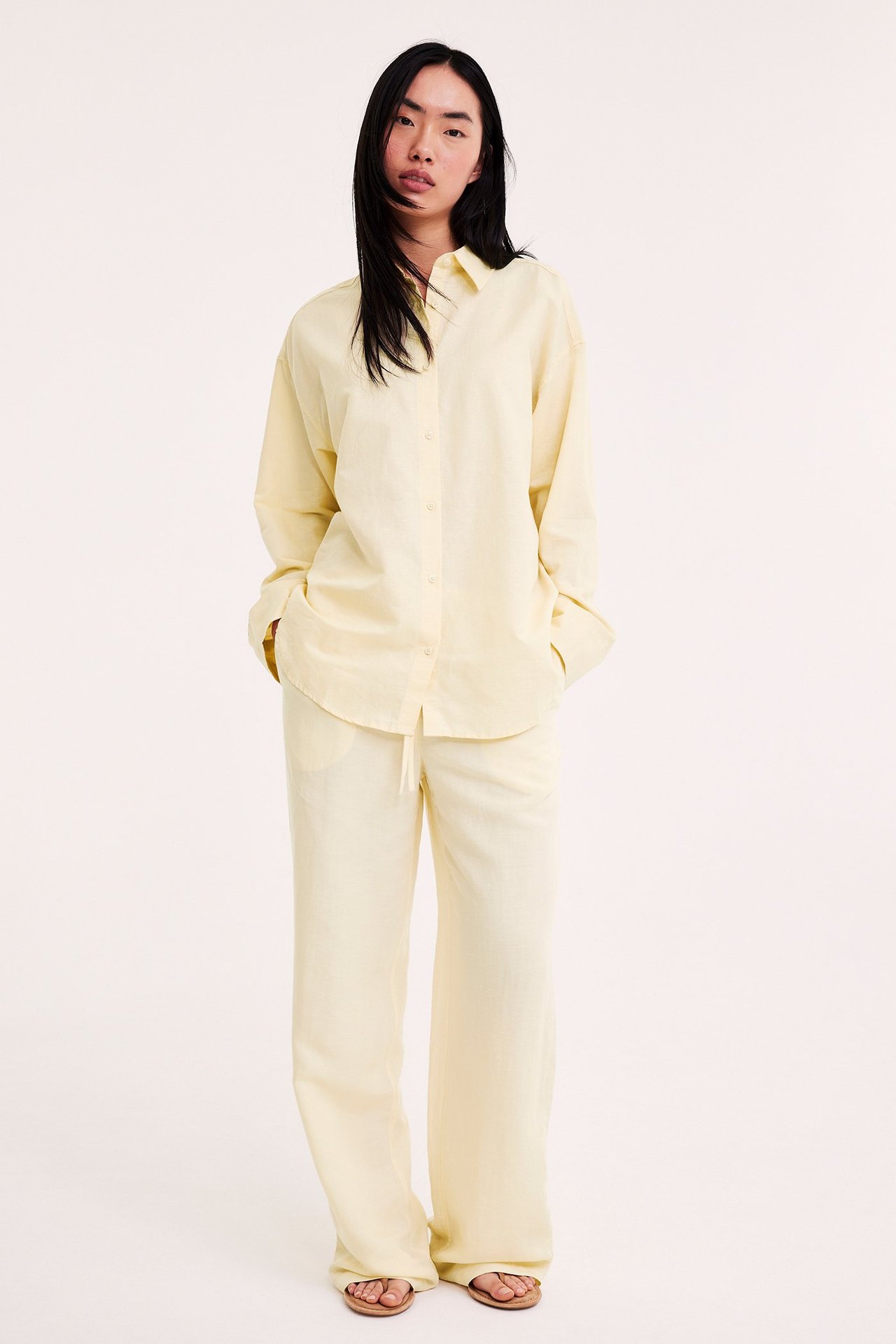 Edestä, nainen yllään väljä vaaleankeltainen pellavasekoitepaita, vastaavat housut ja sandaalit.