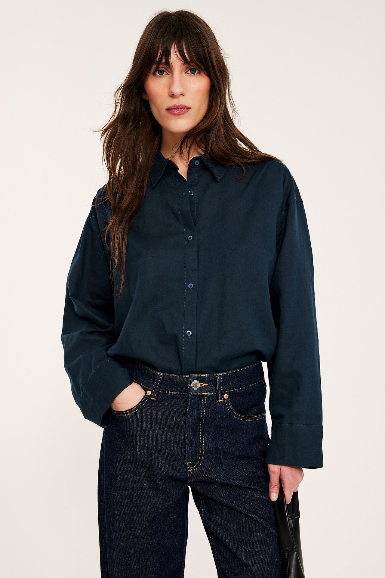 Front: kobieta w oversized ciemnoniebieskiej lnianej koszuli i ciemnych dżinsach, z czarną torebką.