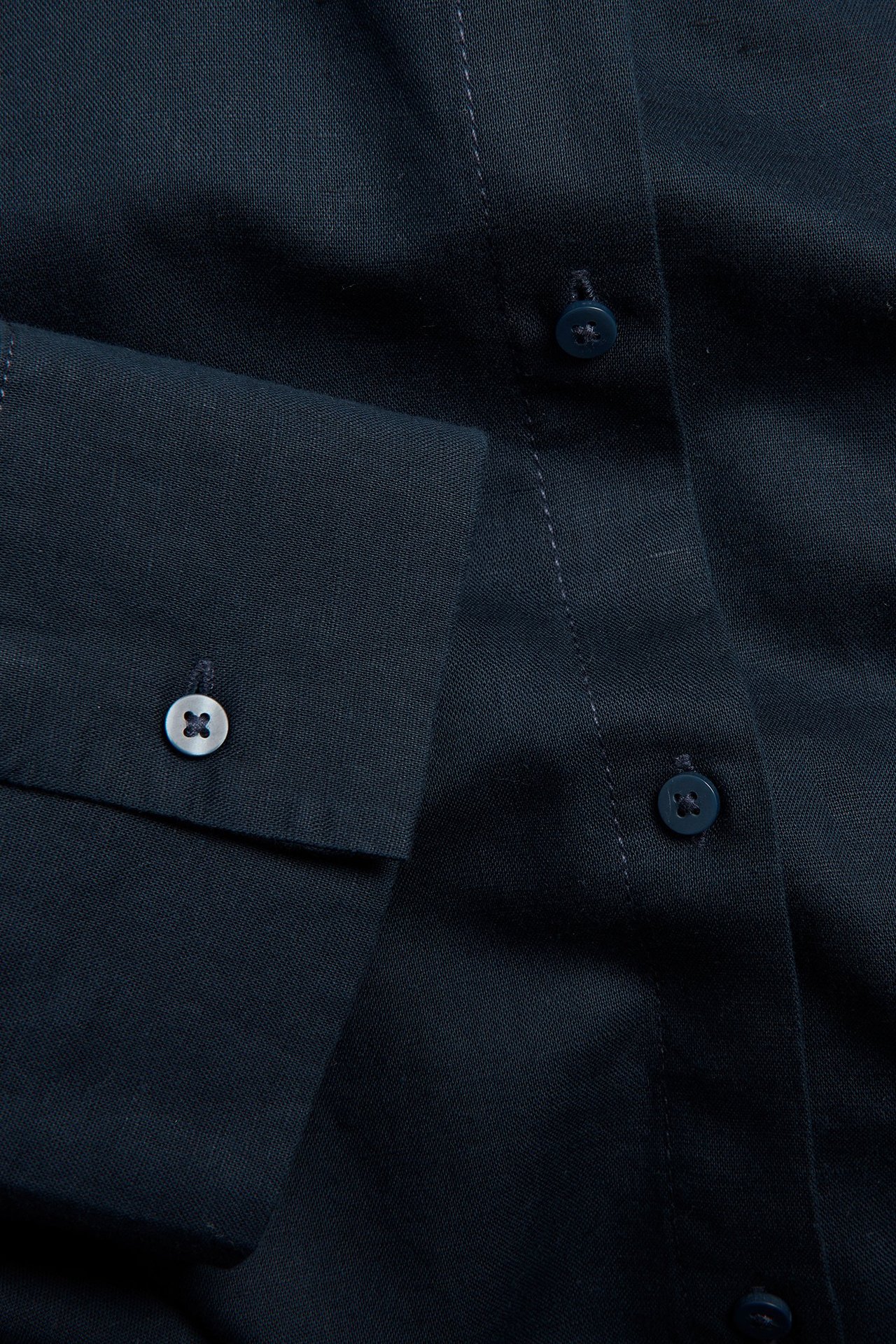 Lähikuva tummansinisestä pellavasekoitepaidasta, jossa nappilista ja vaaleampi nappi hihansuussa.