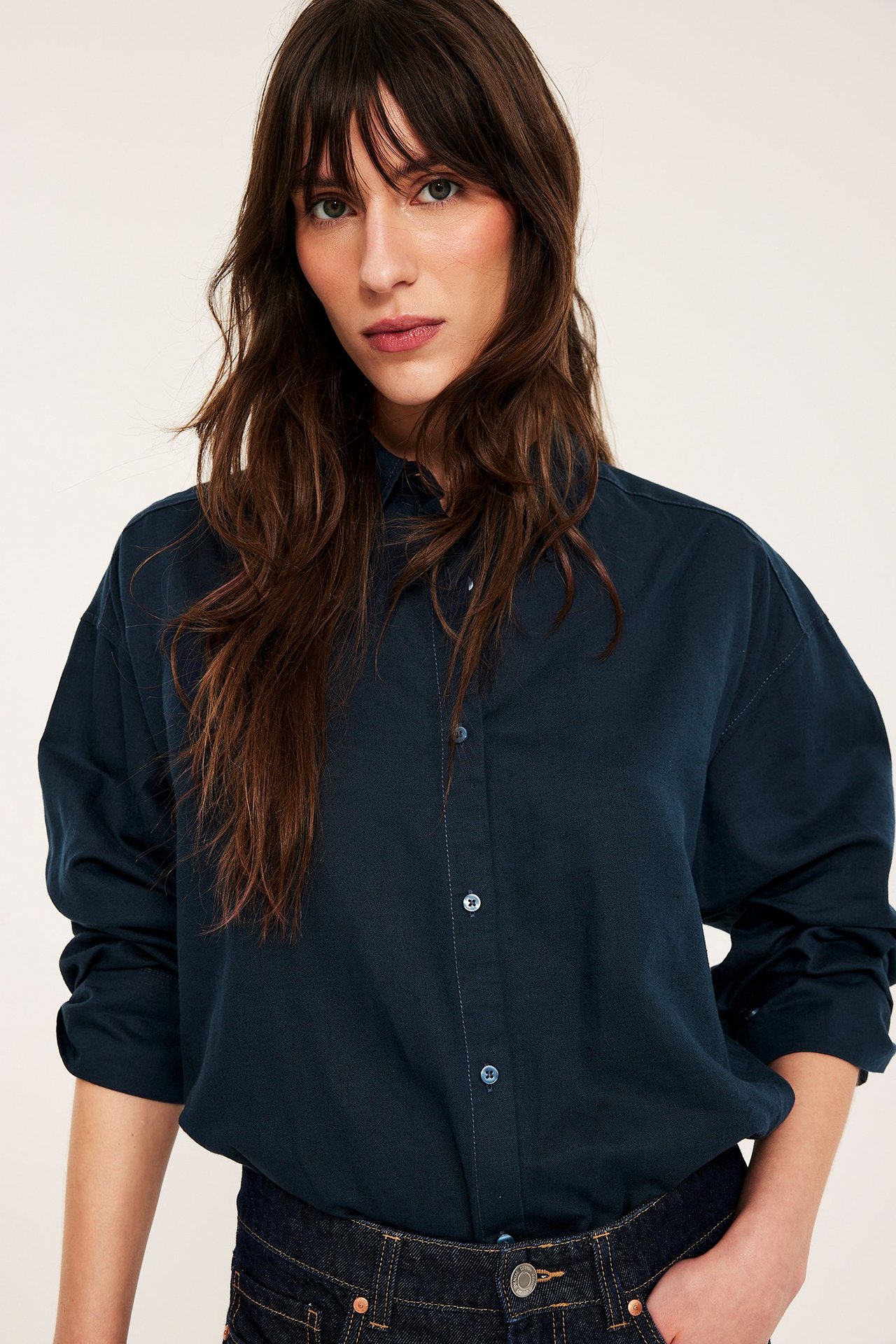 Frontbilde av kvinne i oversized mørkeblå linskjorte med knapping og mørke jeans.