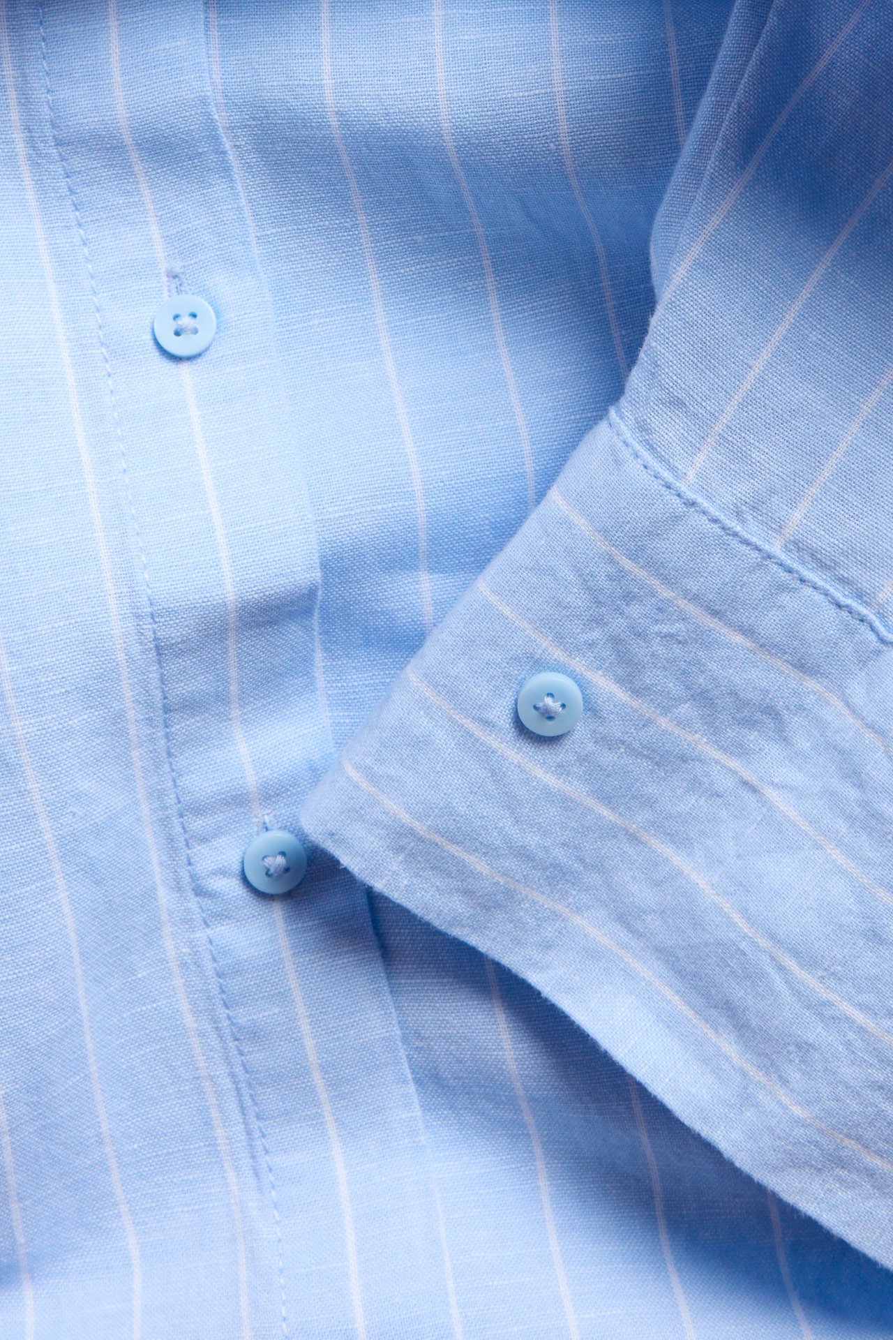 Lähikuva oversized vaaleansinisestä raidallisesta pellavasekoitepaidasta, jossa napit.