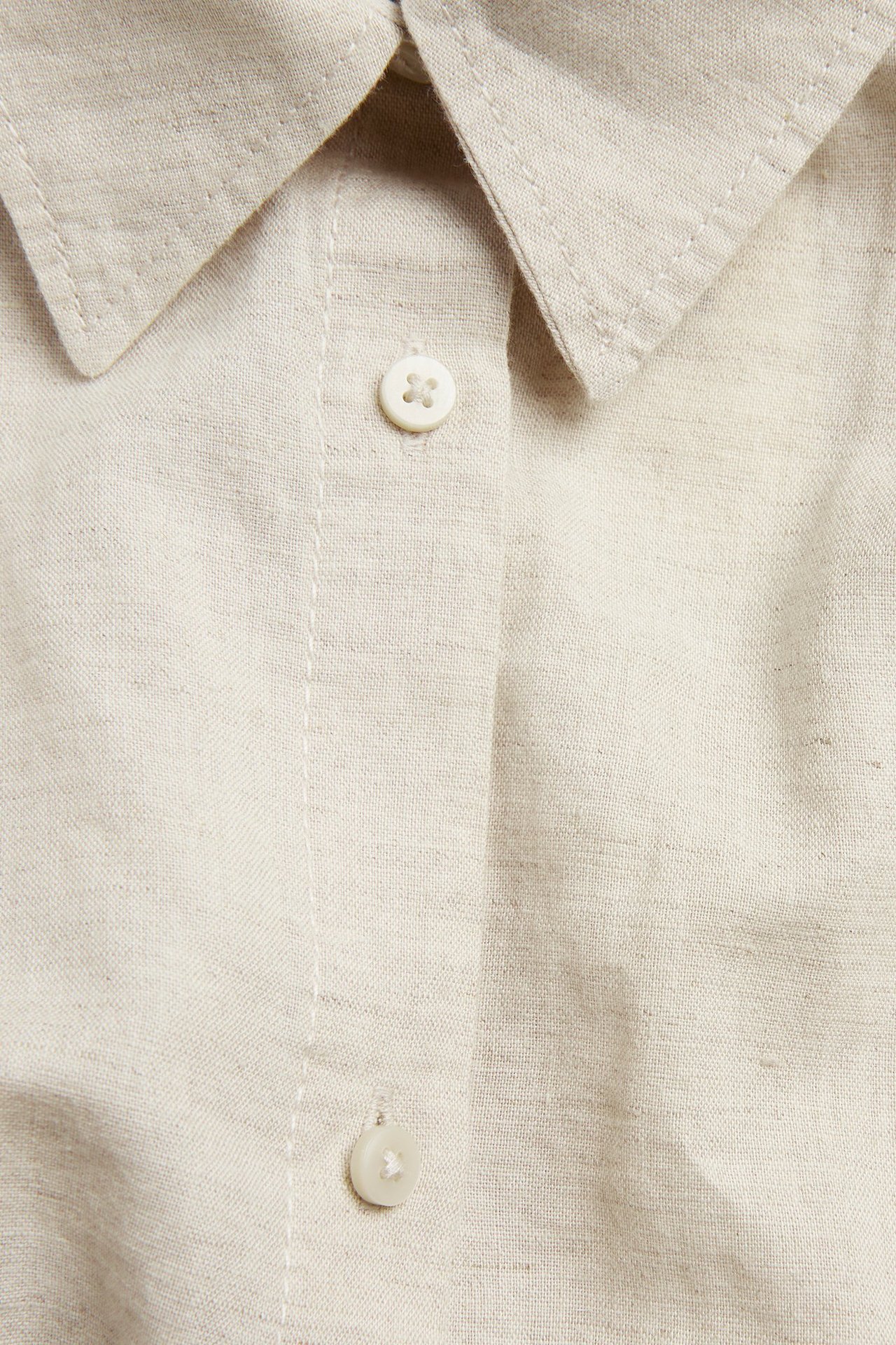 Lähikuva beigestä melange ylisuuresta pellavasekoitepaidasta, jossa on kaulus ja valkoiset napit.