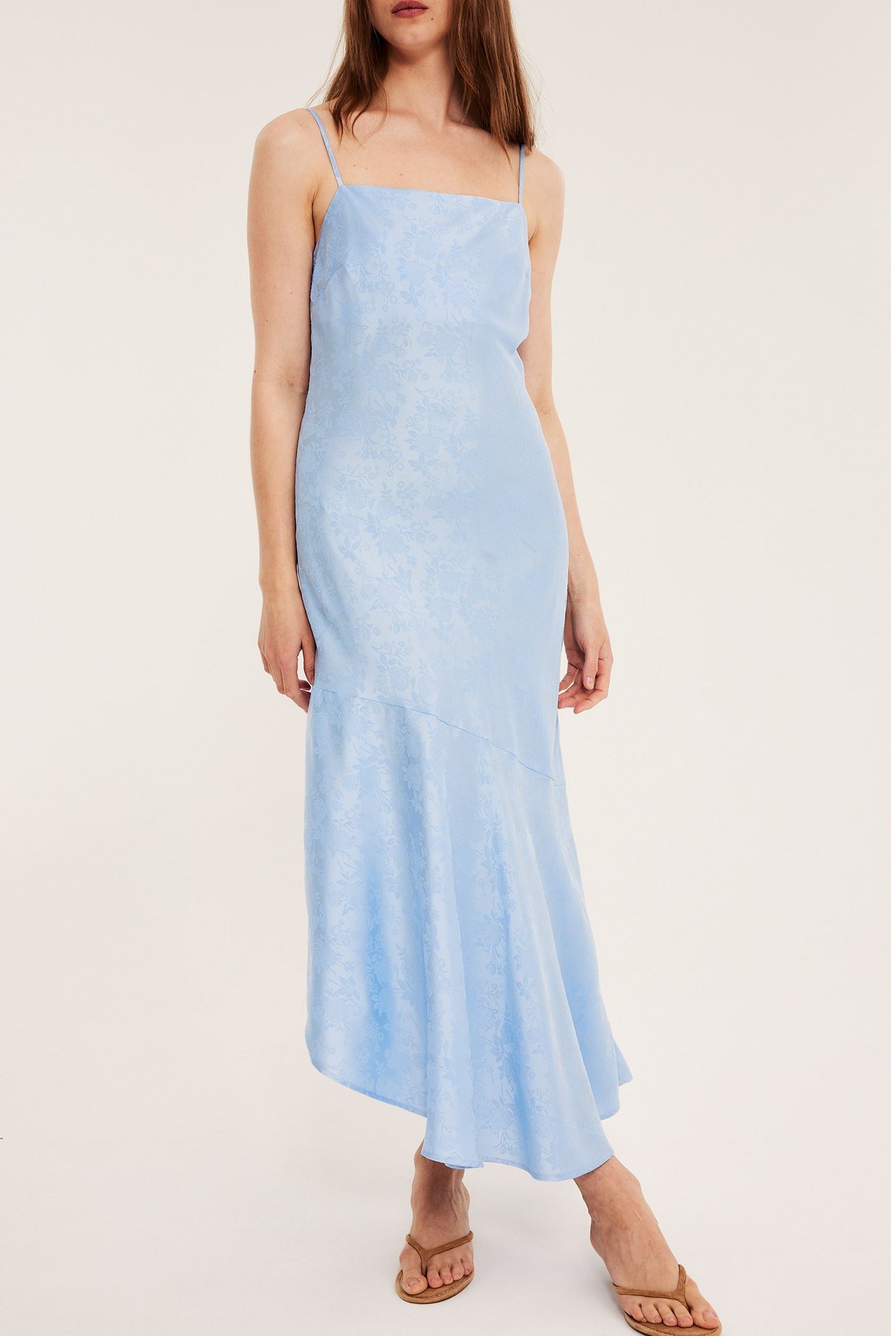 Nainen vaaleansinisessä jacquard-alusmekossa, jossa epäsymmetrinen helma, edestä. Yllään ruskeat sandaalit.