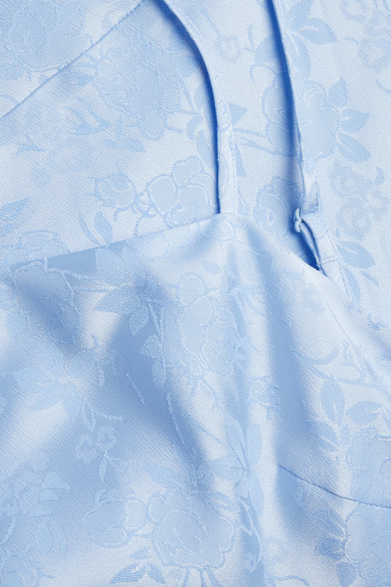 Nærbilde av lyseblå jacquard slipkjolestoff med blomstermønster og en tynn stropp.