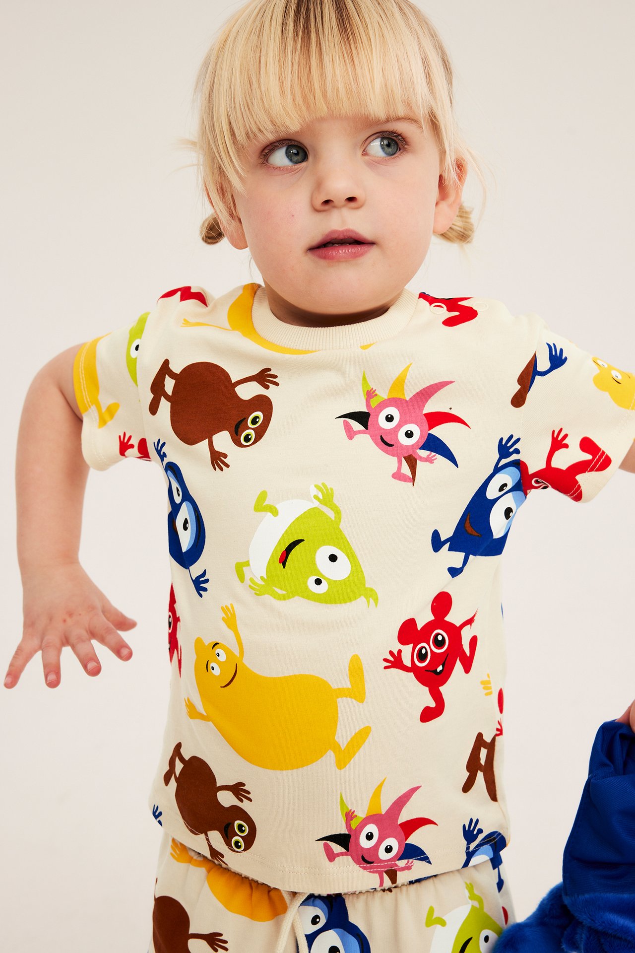 Framifrån: ett barn i ljusbeige bomulls-t-shirt med färgglatt Babblarna-tryck och matchande mönstrade underdel.