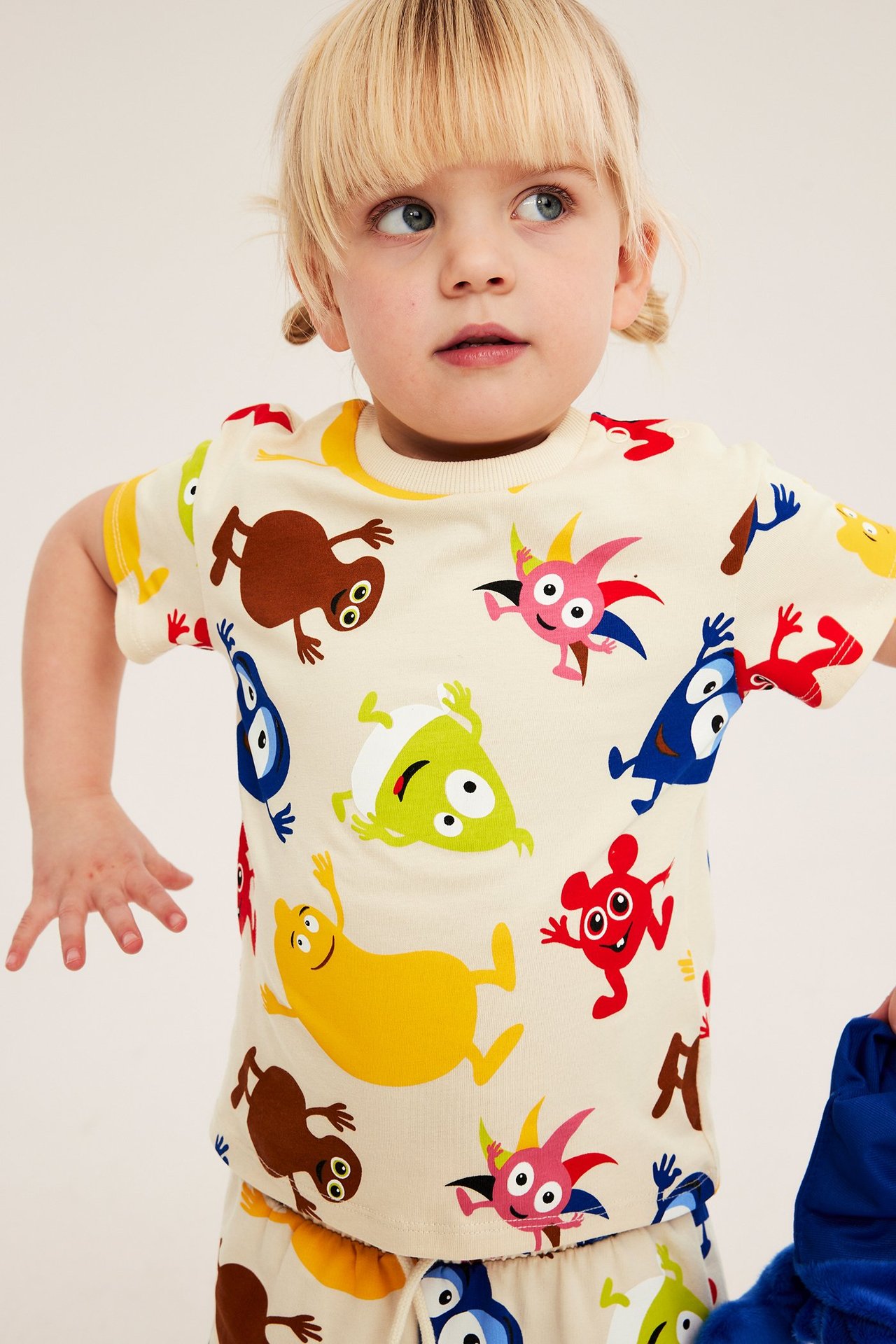 Widok z przodu: dziecko w jasnobeżowej bawełnianej koszulce z nadrukiem Babblarna i pasującymi spodenkami.