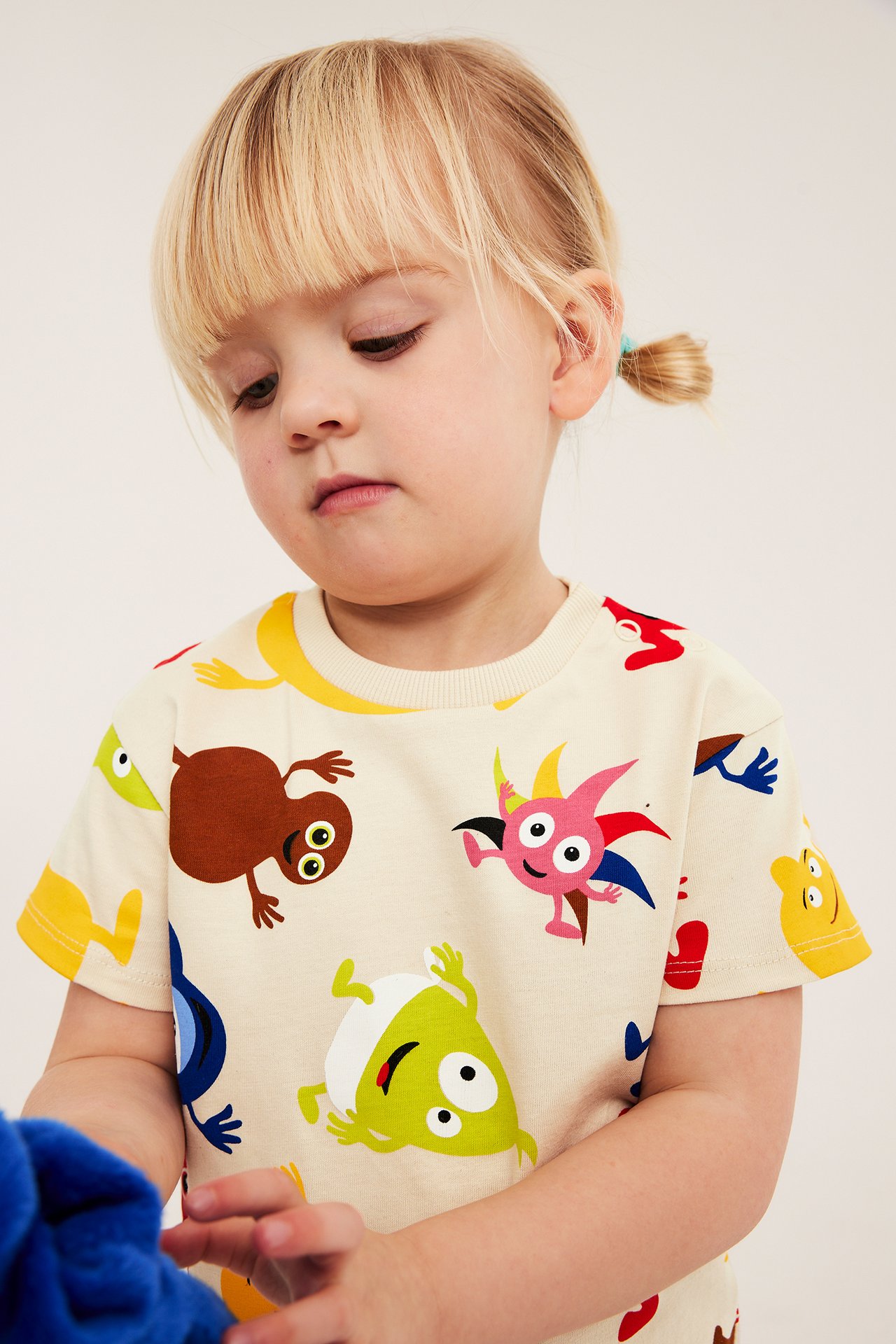 Närbild på en barns ljusbeige bomulls-t-shirt med färgglatt Babblarna-tryck och axelknappar.