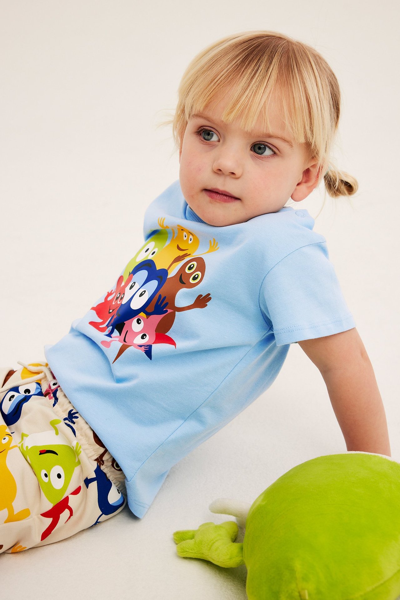 Zbliżenie dziecka w jasnoniebieskiej bawełnianej koszulce z nadrukiem Babblarna i wzorzystych beżowych szortach.