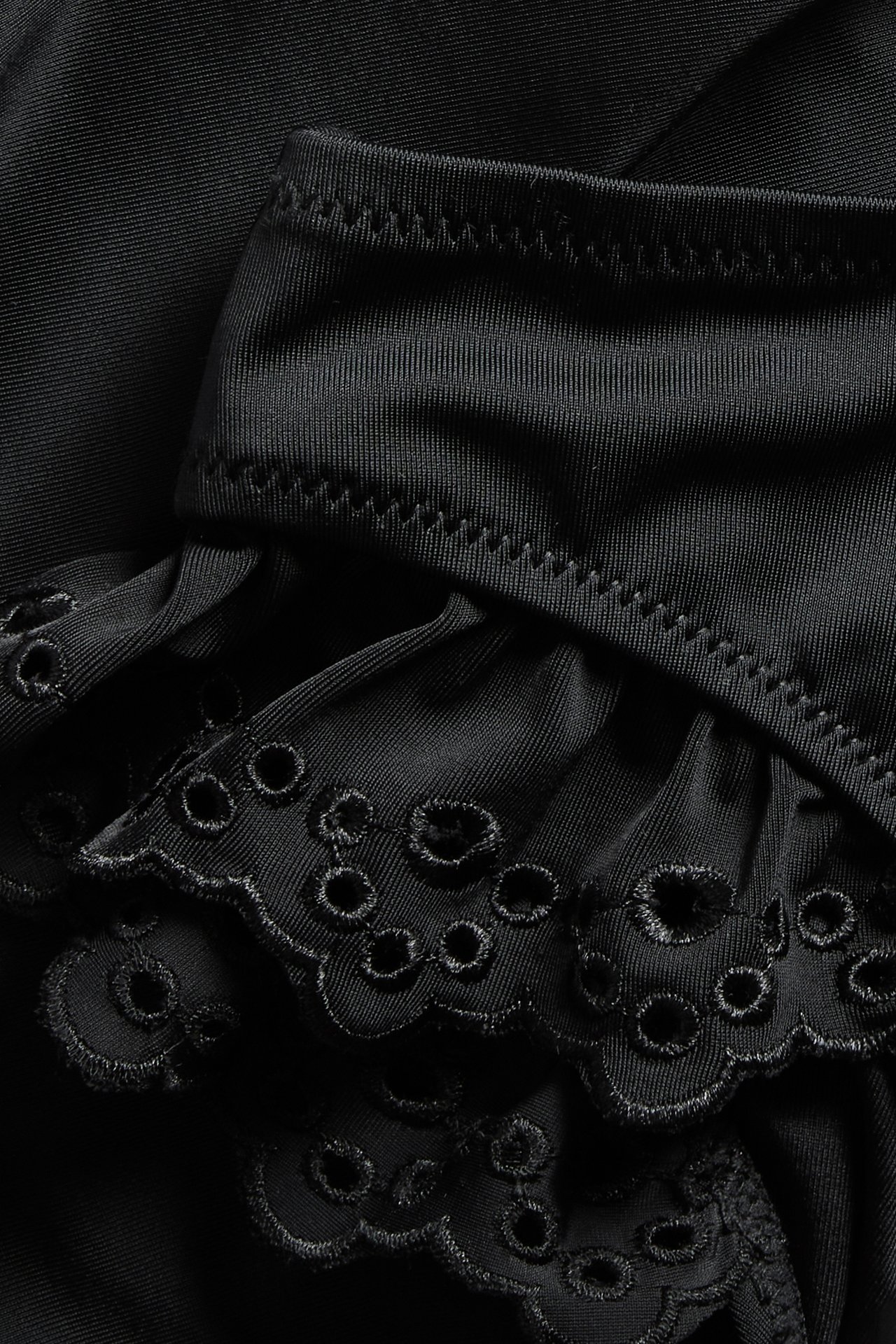 Zbliżenie na czarne majtki kąpielowe typu brazilian z falbanami i haftem angielskim.