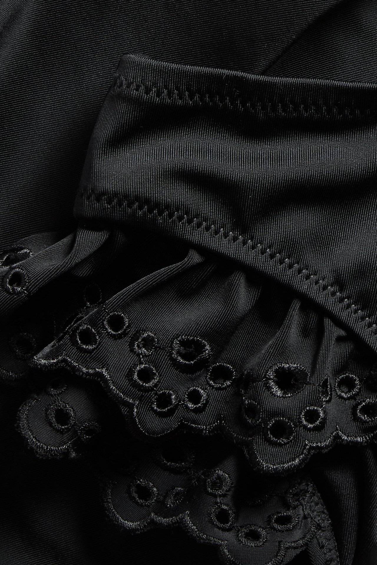 Zbliżenie na czarne majtki kąpielowe typu brazilian z falbanami i haftem angielskim.