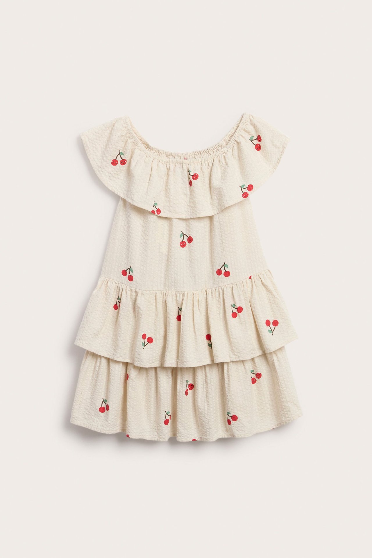 Frontbilde av en beige barnekjole i seersucker med volanger og kirsebærtrykk.