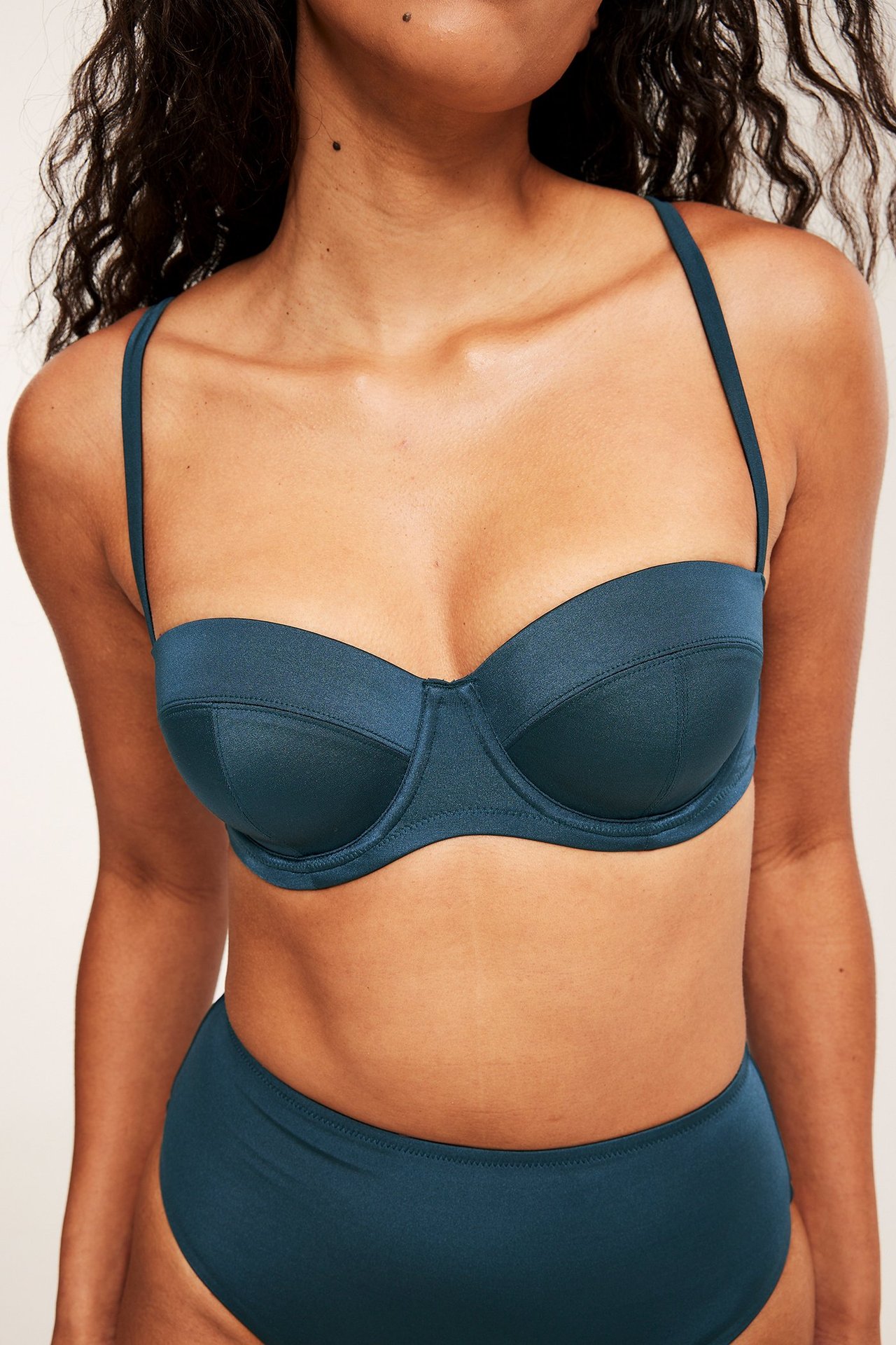 Naisen etunäkymä tummansinisessä kaarituellisessa balconette-bikinitopissa ja yhteensopivissa alaosissa.