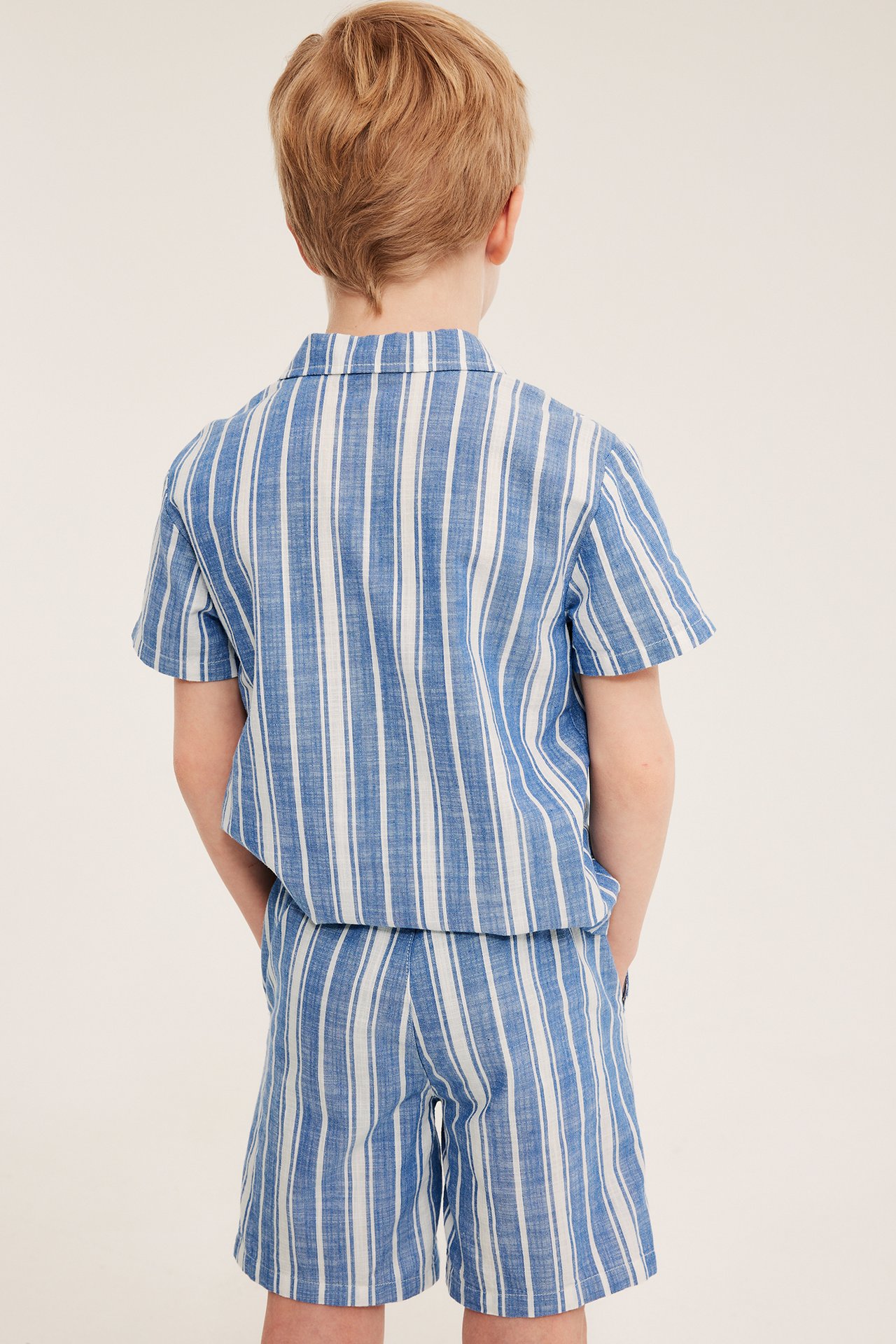 Lapsi selin, yllään sinivalkoraidalliset puuvillashortsit ja niihin sopiva lyhythihainen paita.