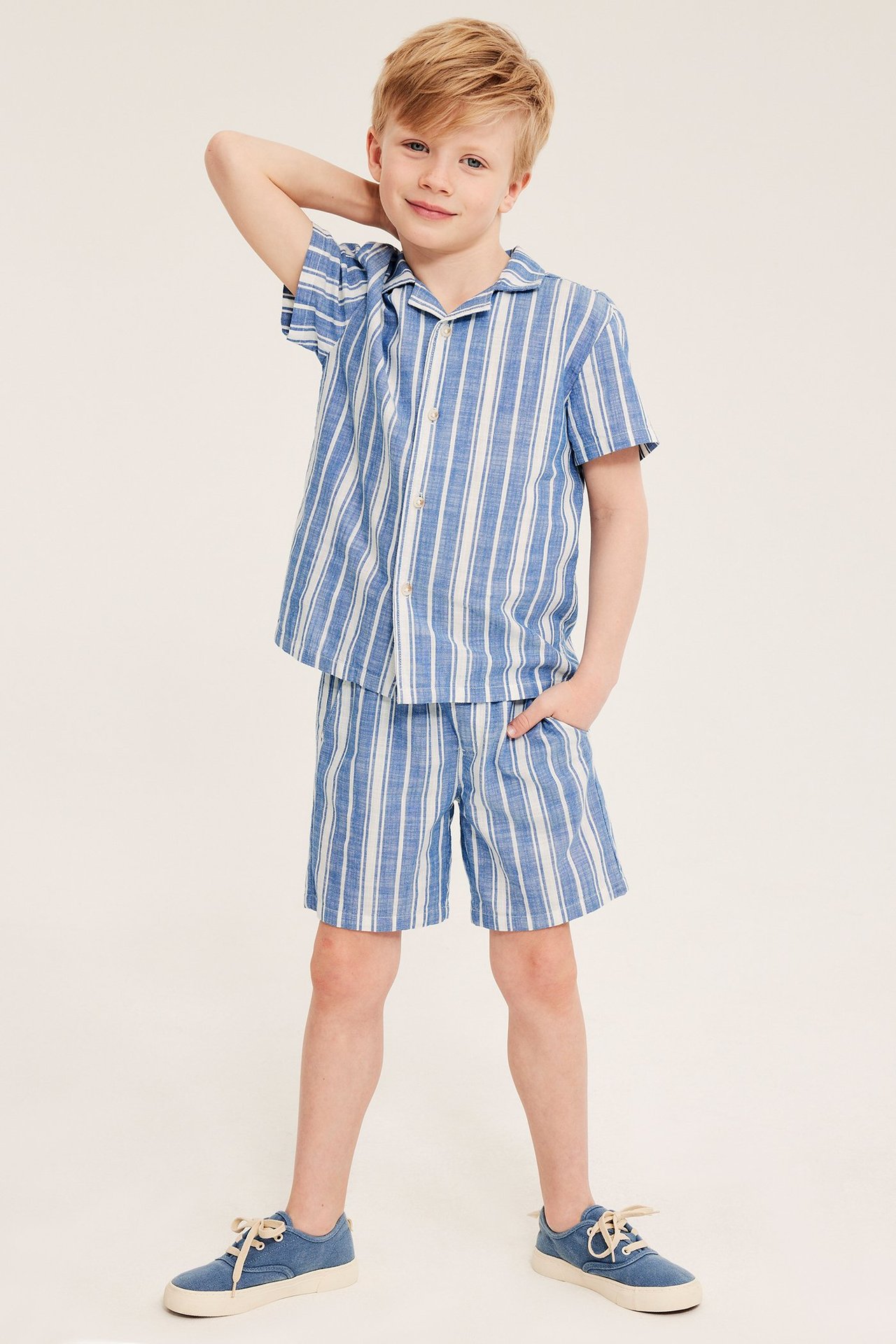 Lapsi edestä: tummansiniset ja valkoraidalliset puuvillashortsit, yhteensopiva paita ja siniset tennarit.