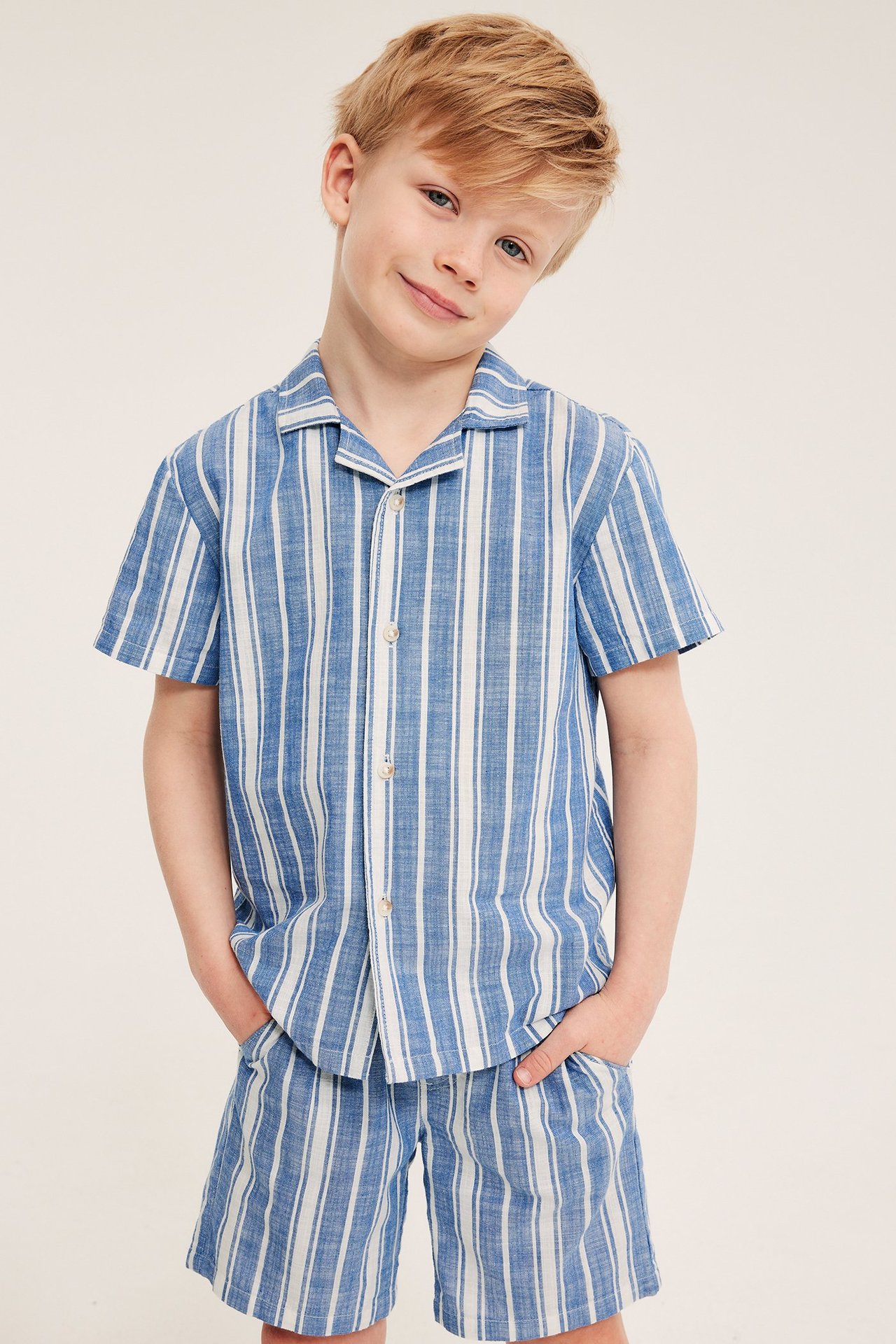 Edestä: Lapsi yllään tummansiniset, valkoraitaiset pehmeät puuvillashortsit ja yhteensopiva paita.