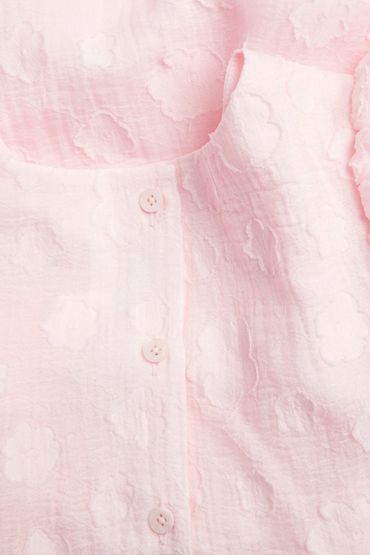 Zbliżenie jasnoróżowej sukienki z organzy, z kwiatowym wzorem 3D i guzikami z przodu.