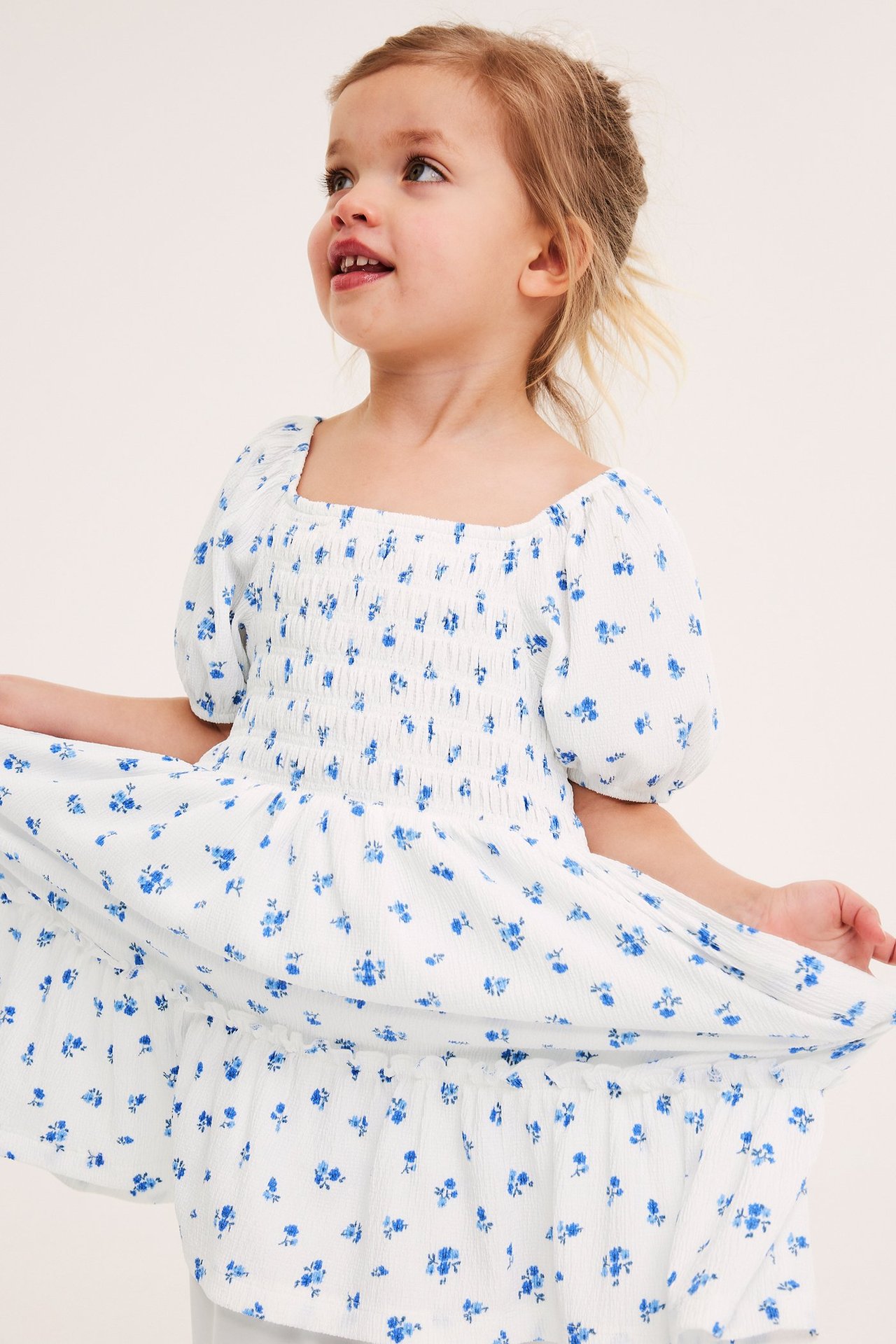 Framifrån en flicka i en offwhite krinklad jerseymönstrad klänning med smockat liv och puffärmar.