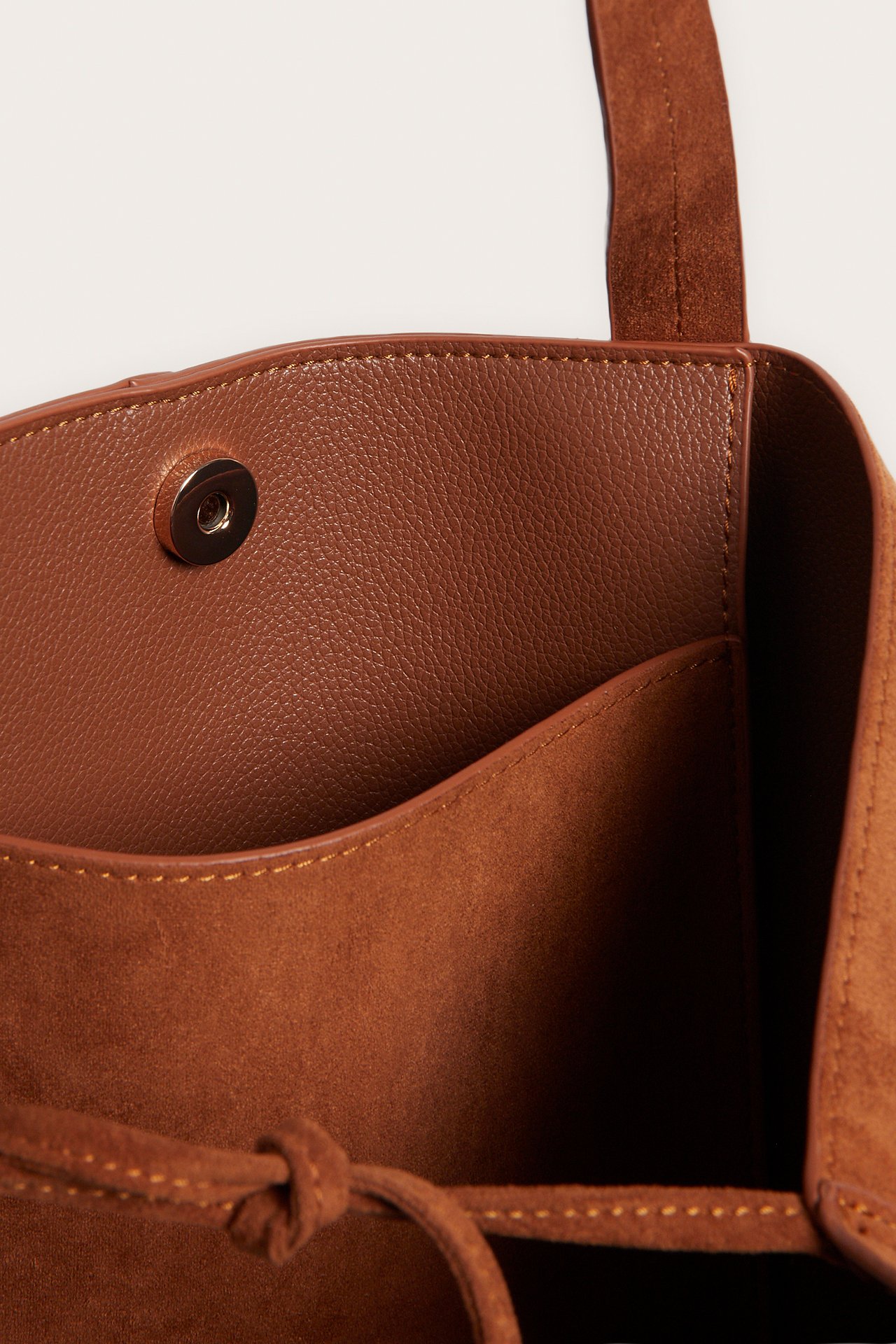 Nærbilde av en brun semsket imitert skinnveske med magnetlås og innerlomme.