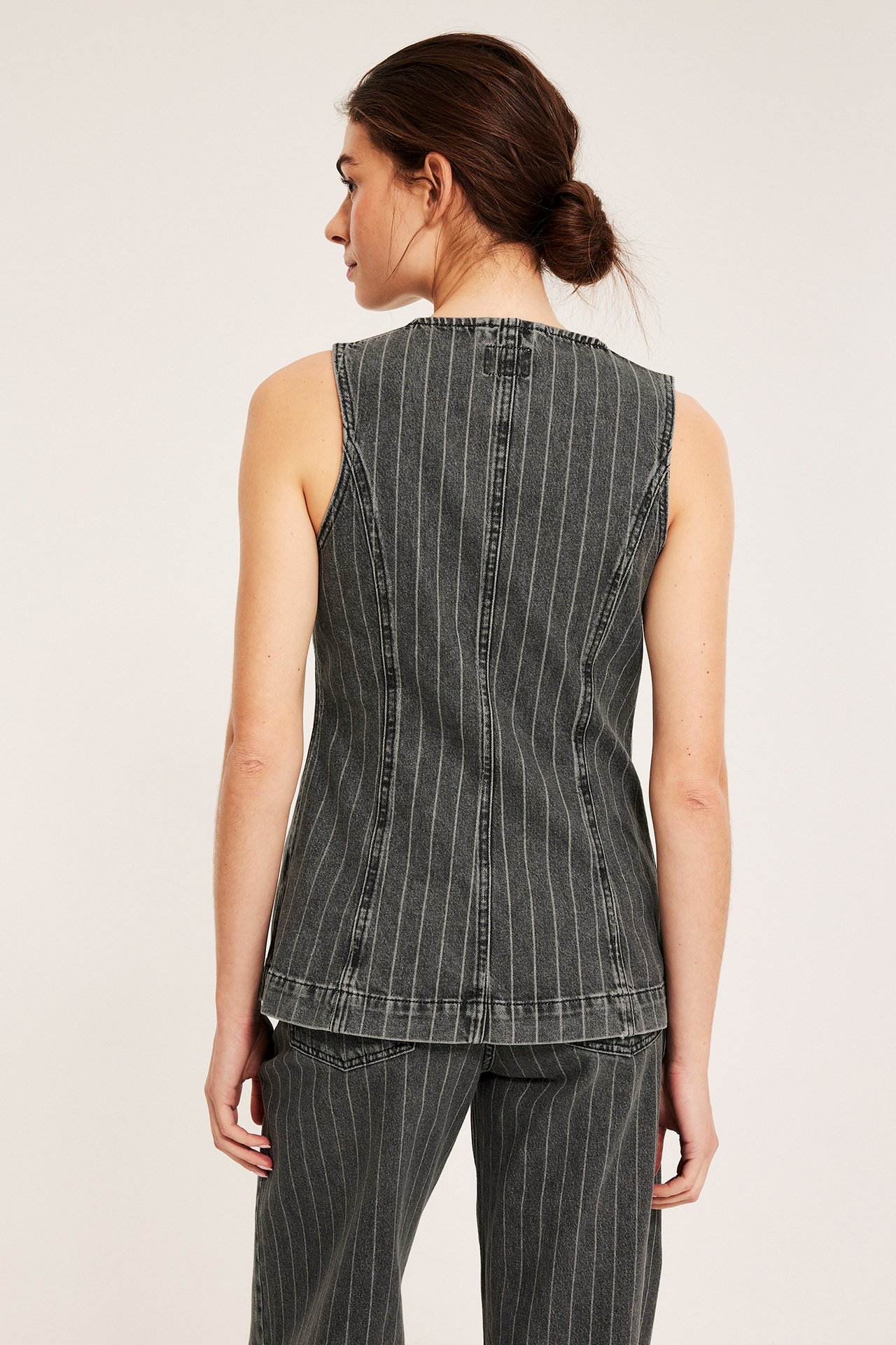 Naisen takakuva tummanharmaassa raidallisessa, istuvassa farkkuliivissä ja yhteensopivissa farkuissa.