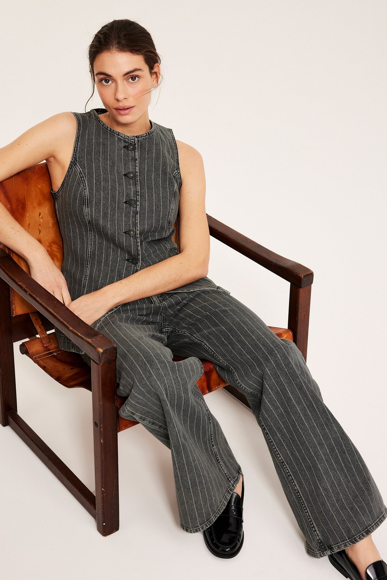 Forfra: kvinne i mørkegrå stripete denimvest, matchende vide jeans og svarte loafers.