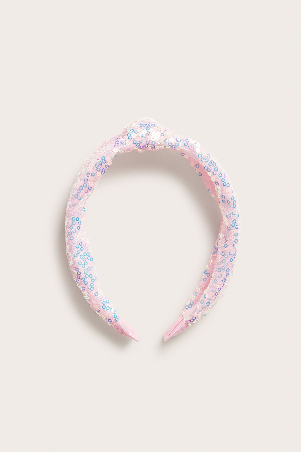Ovenfra, et rosa hårbånd med en dekorativ knute, dekket av skimrende paljetter.