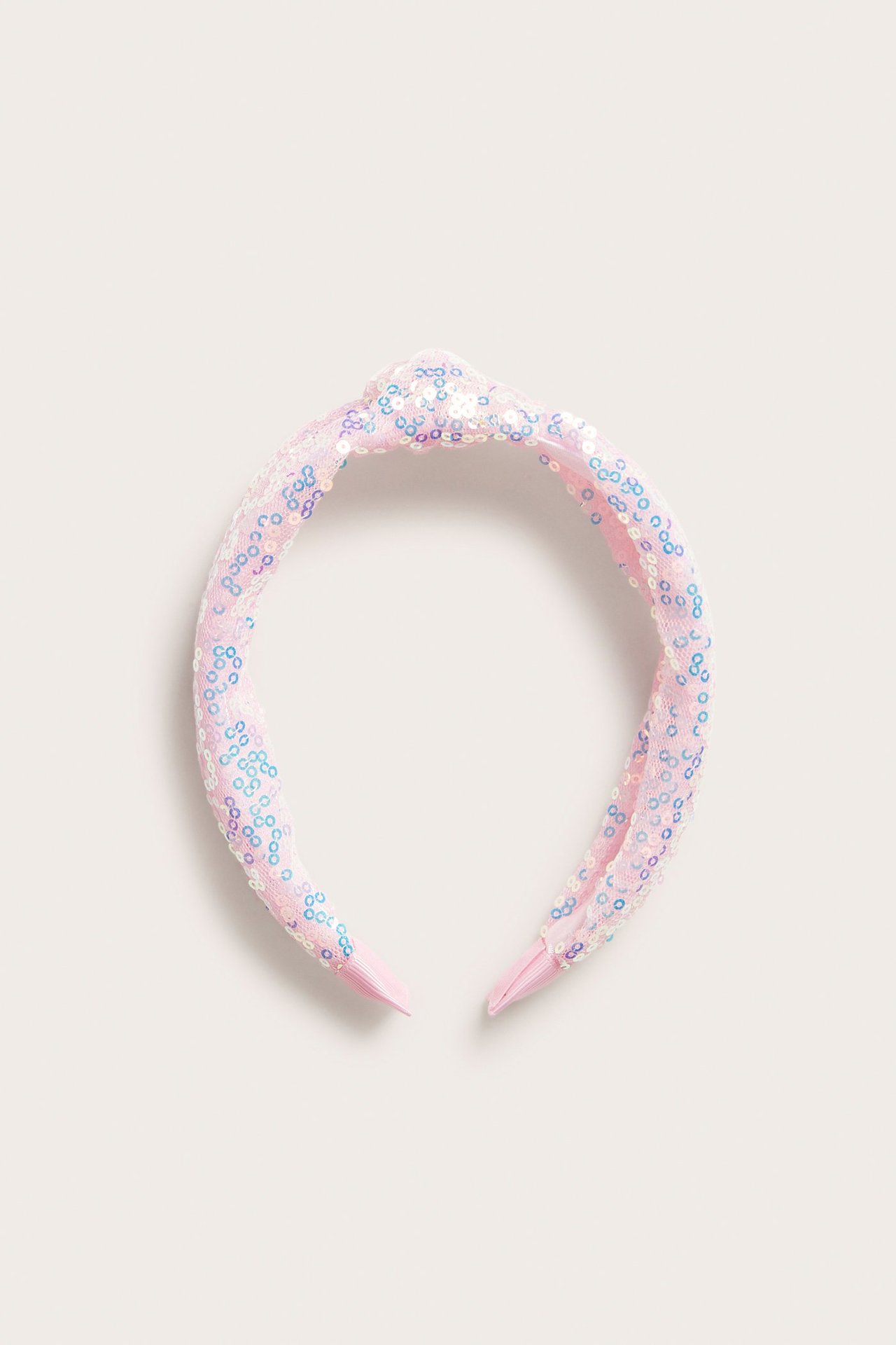 Widok z przodu różowej opaski na głowę z ozdobnym węzłem, pokrytej błyszczącymi cekinami.