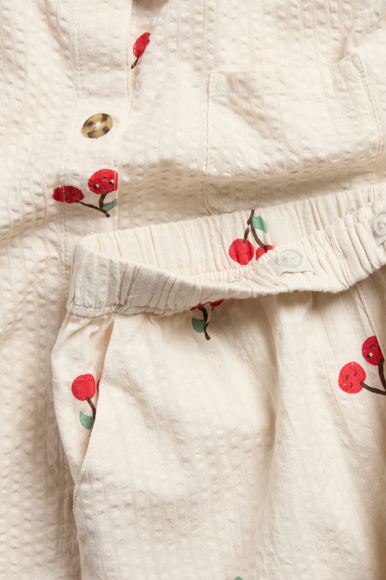 Zbliżenie beżowej koszuli z seersuckeru w wiśnie z guzikami, w zestawie z pasującymi elastycznymi szortami.