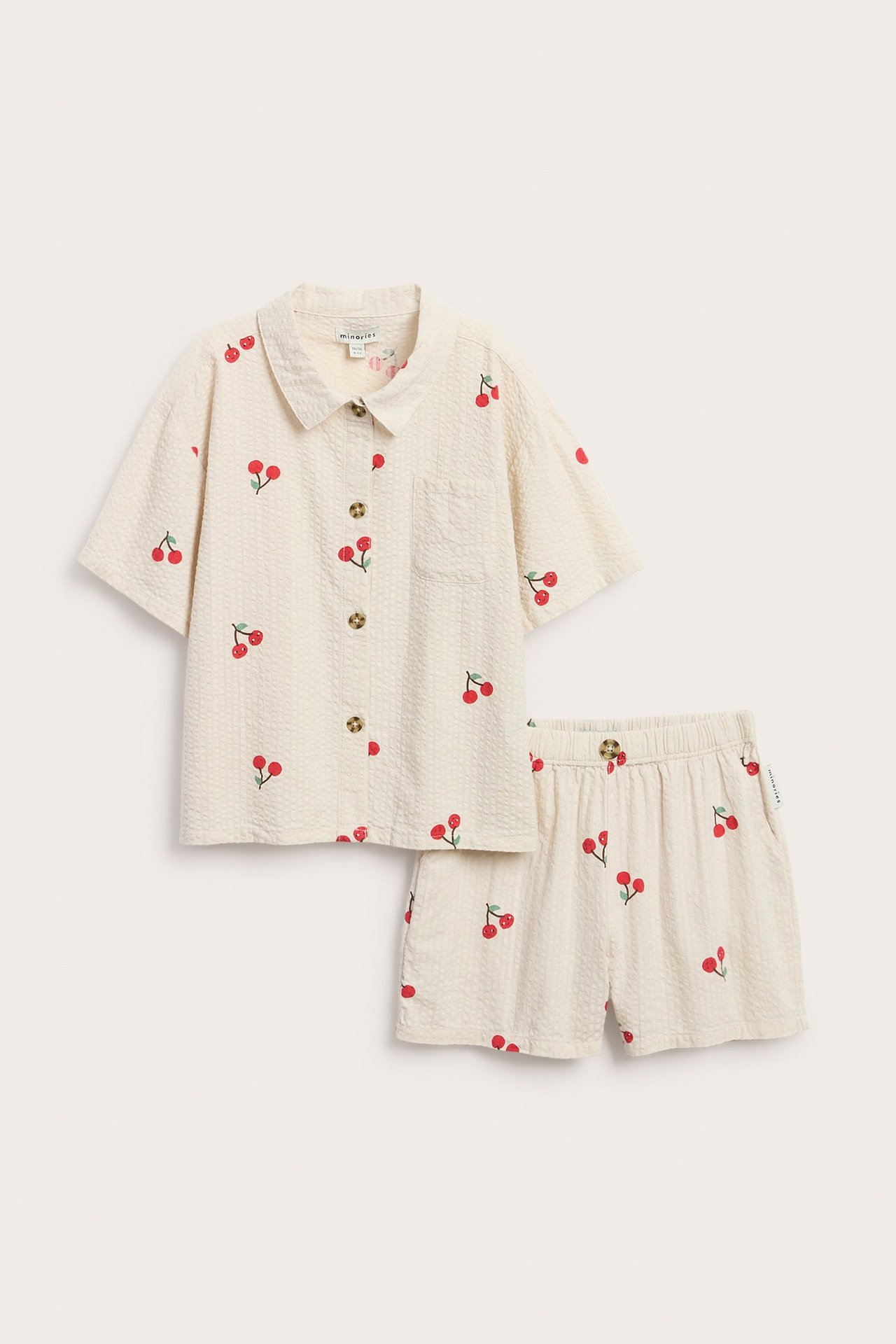 Widok z przodu dziecięcego beżowego zestawu z seersuckeru: koszula w wisienki z krótkim rękawem i pasujące szorty.