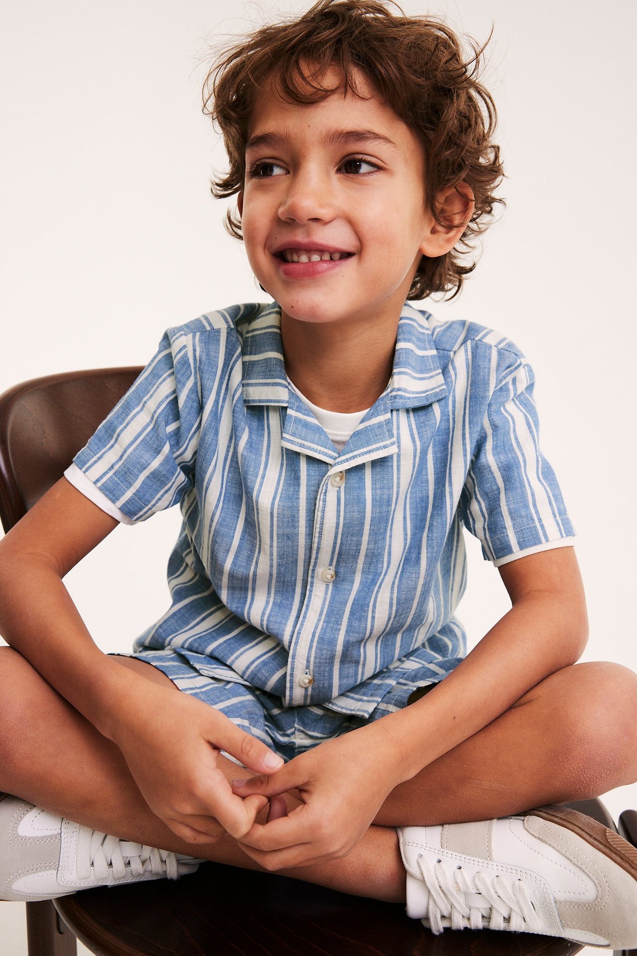 Frontvy: Ett barn bär en mörkblå och vitrandig kortärmad bomullsskjorta med matchande shorts.