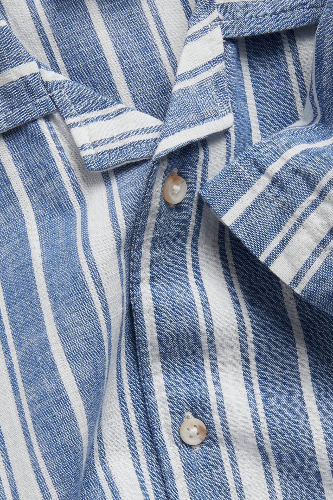 Zbliżenie: granatowo-biała, pasiasta bawełniana koszula z krótkim rękawem i guzikami.