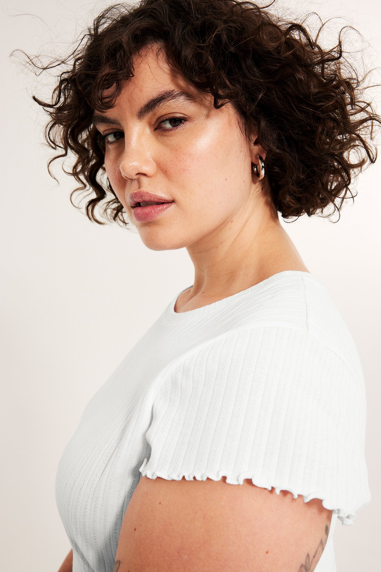 Zbliżenie, widok z boku kobiety w białym t-shircie pointelle z rękawami babylock i złotymi kolczykami kołami.