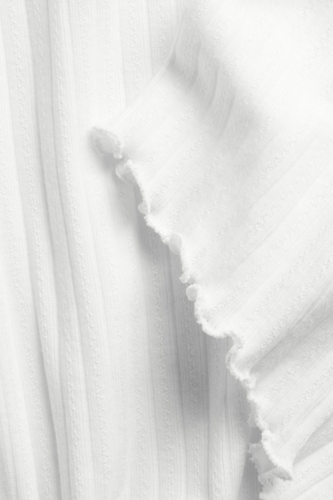 Zbliżenie na biały, bawełniany T-shirt pointelle ze wzorzystą fakturą i obszyciem typu babylock.