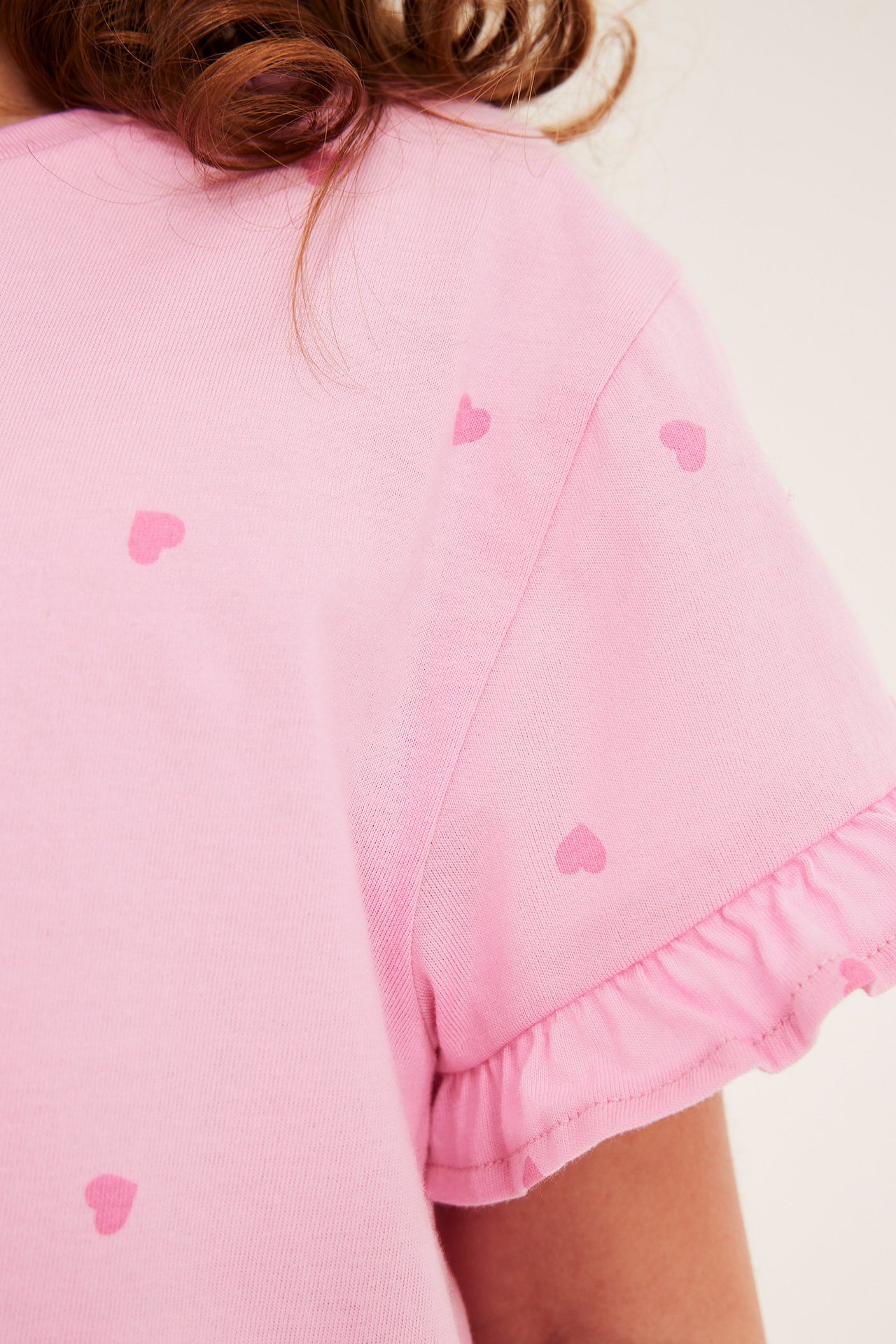 Lähikuva, lapsi yllään vaaleanpunainen puuvillainen t-paita sydänkuviolla ja röyhelöhihoilla.