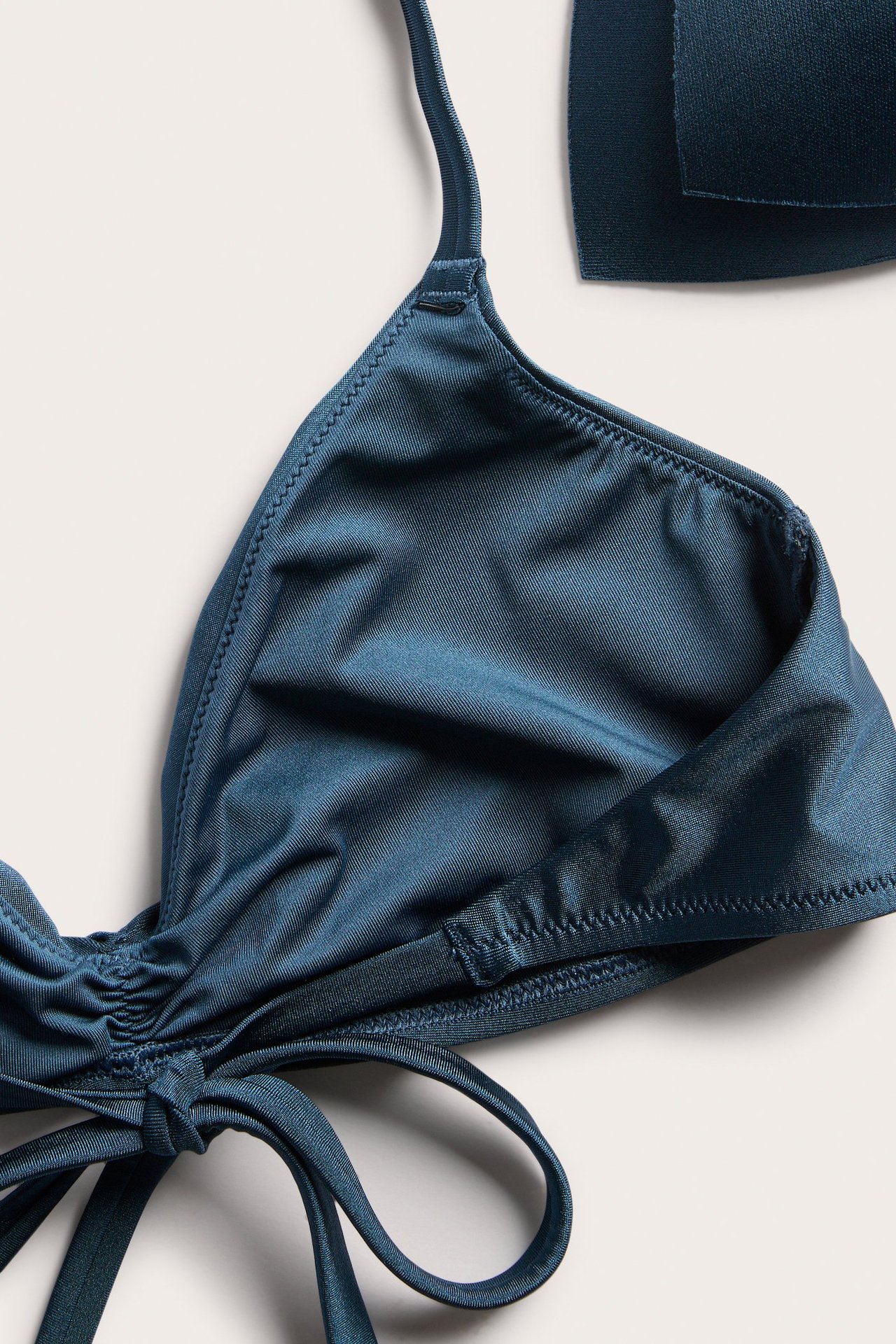 Nærbilde av en mørkeblå polstret trekant-bikinitopp med knyting foran og rynkedetaljer.