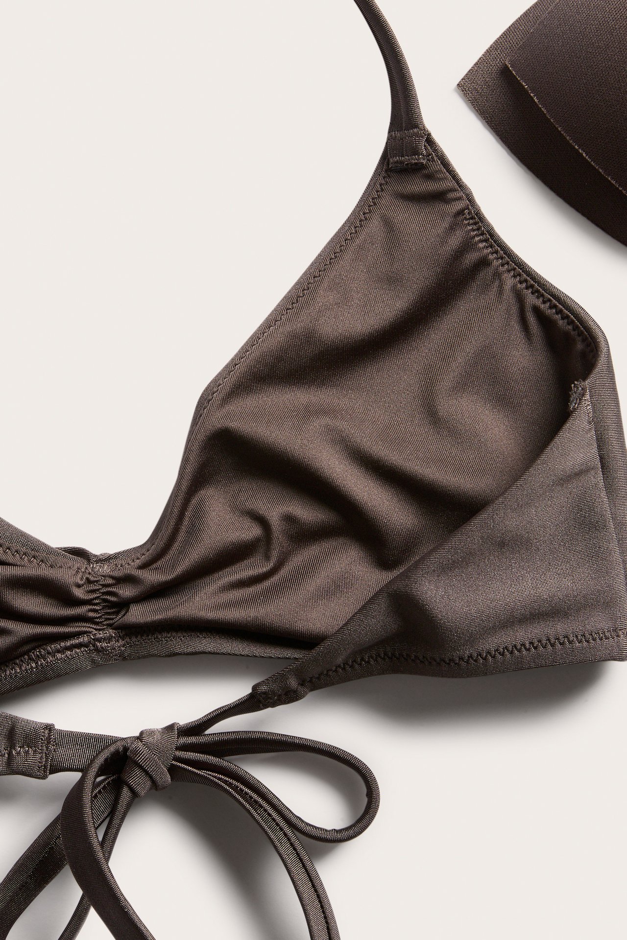 Nærbilde: brun vattert trekantbikinitopp med rynkedetaljer, knytebånd og uttakbar polstring.