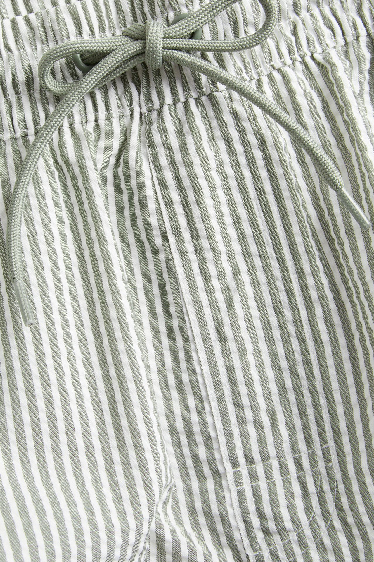 Närbild av randiga mörkgröna och vita bäckebölja-badshorts för herr med resår och dragsko i midjan.