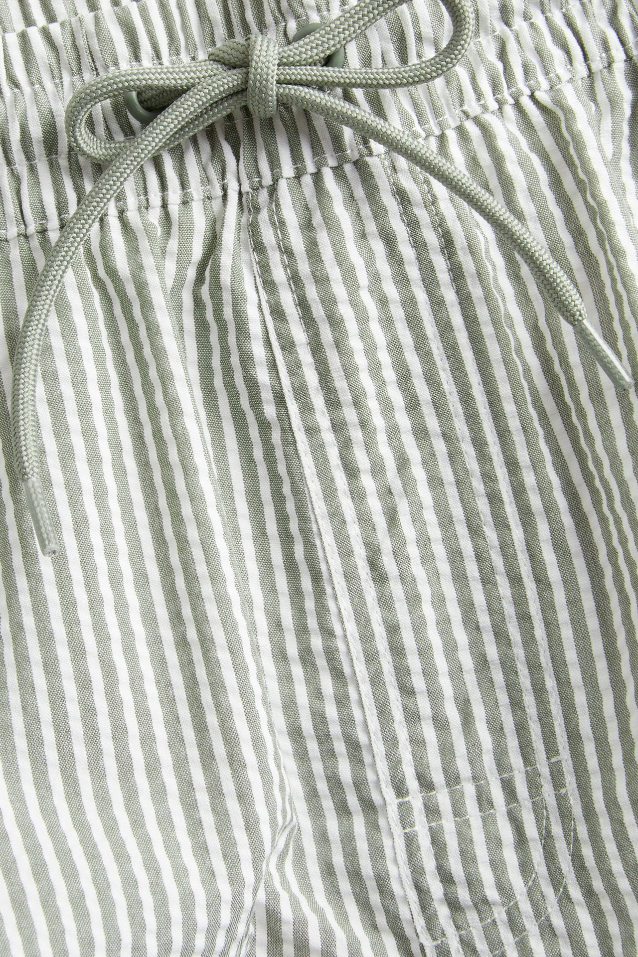 Zbliżenie na męskie ciemnozielone i białe paski szortów kąpielowych z seersuckeru z elastycznym pasem na sznurek.