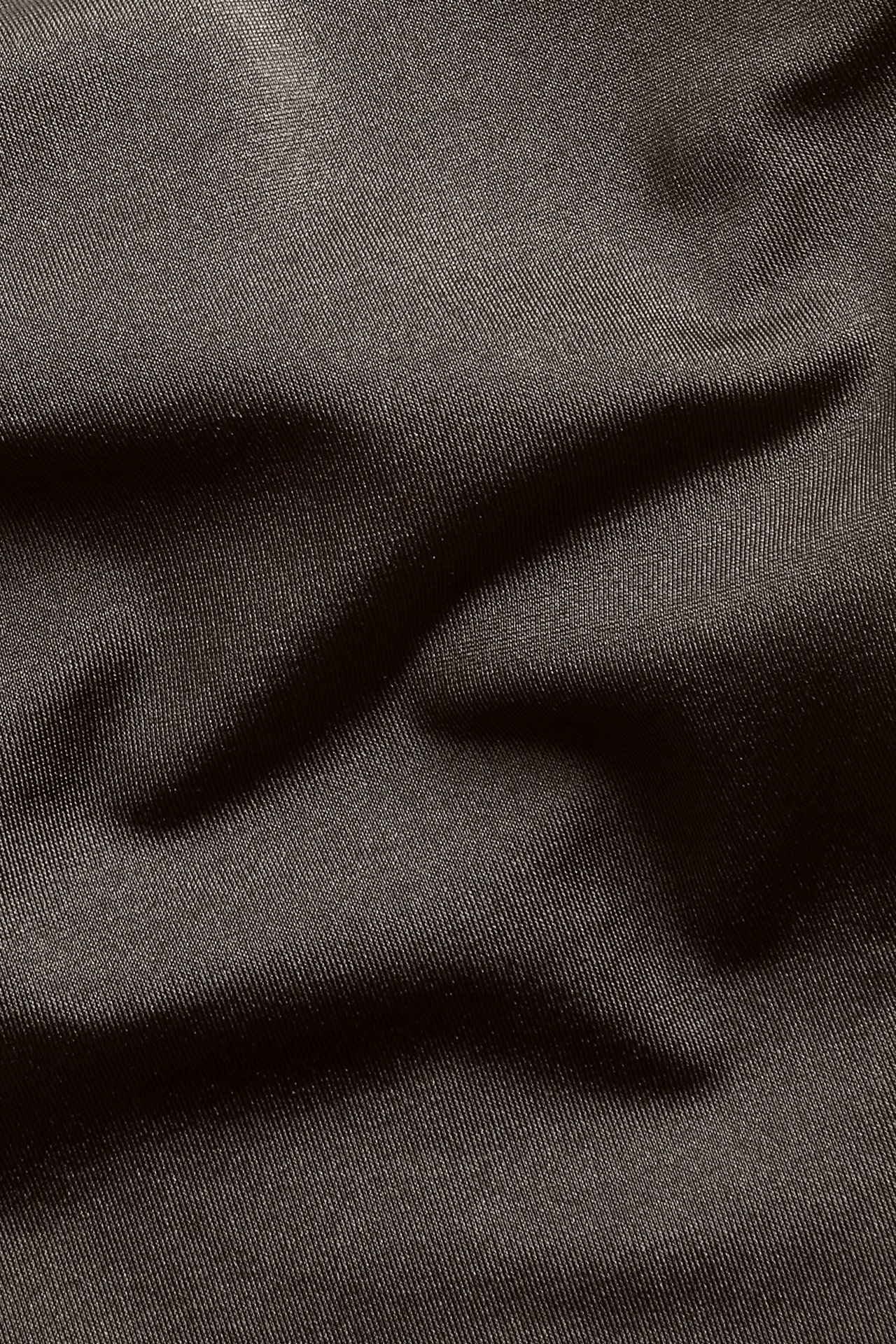 Lähikuva ruskeasta, yksivärisestä bikinikankaasta, jossa on hienovaraista tekstuuria ja taitoksia.