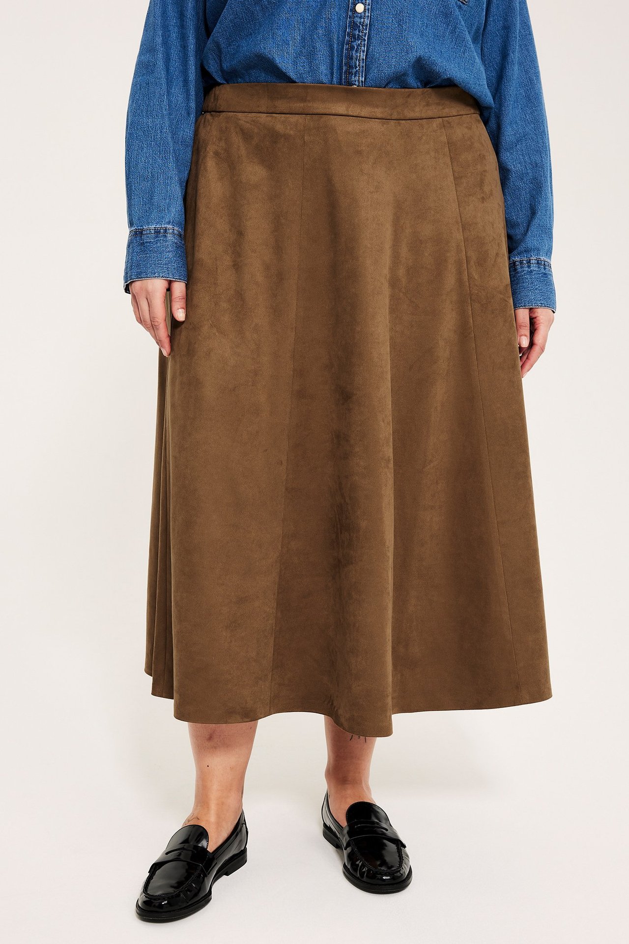 Naisen etunäkymä ruskeassa mokkajäljitelmä-midihameessa, sinisessä farkkupaidassa ja mustissa kiiltonahkakengissä.